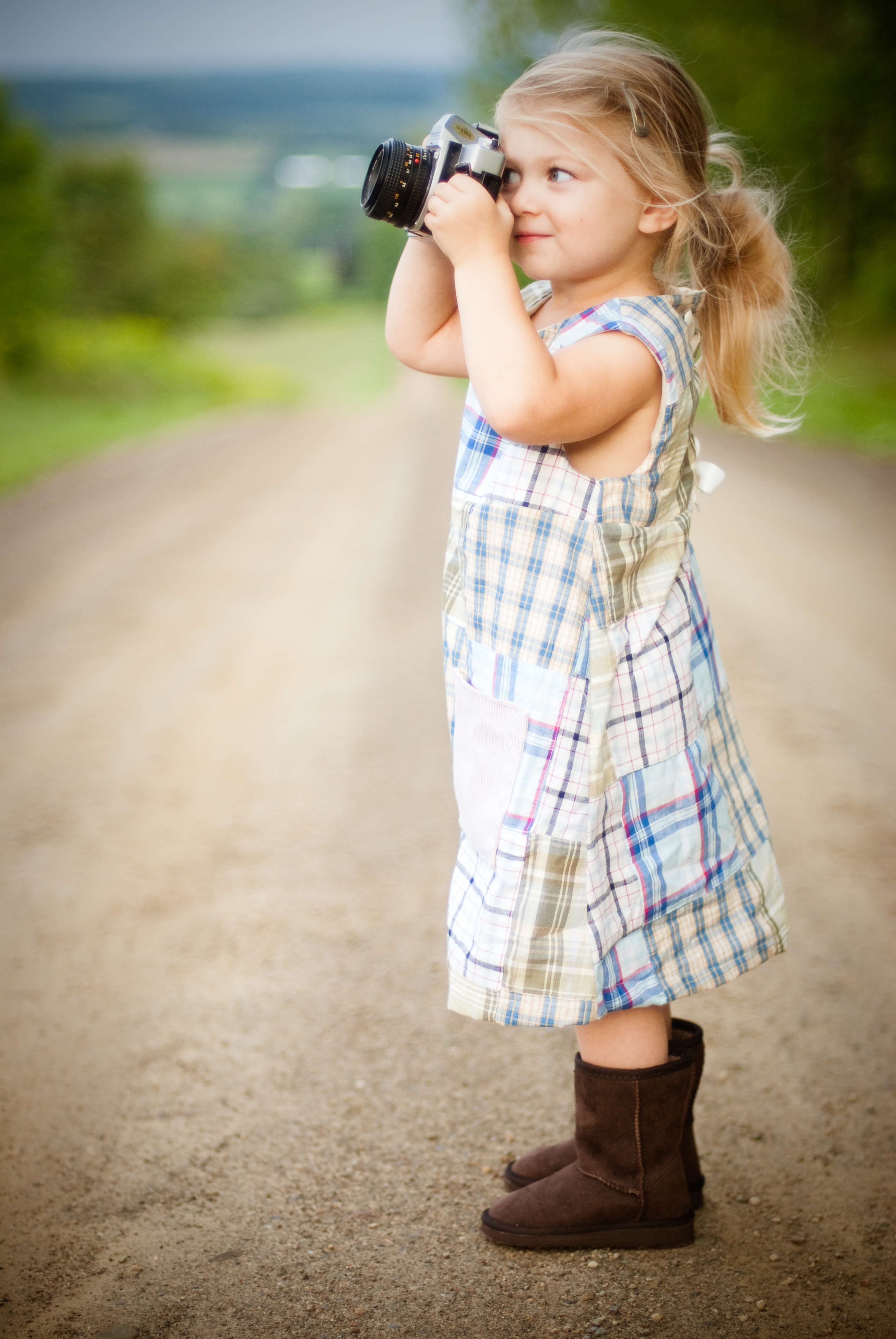 Girl with blonde hair and wearing blue and white plaid dress and capturing picture during daytime photo