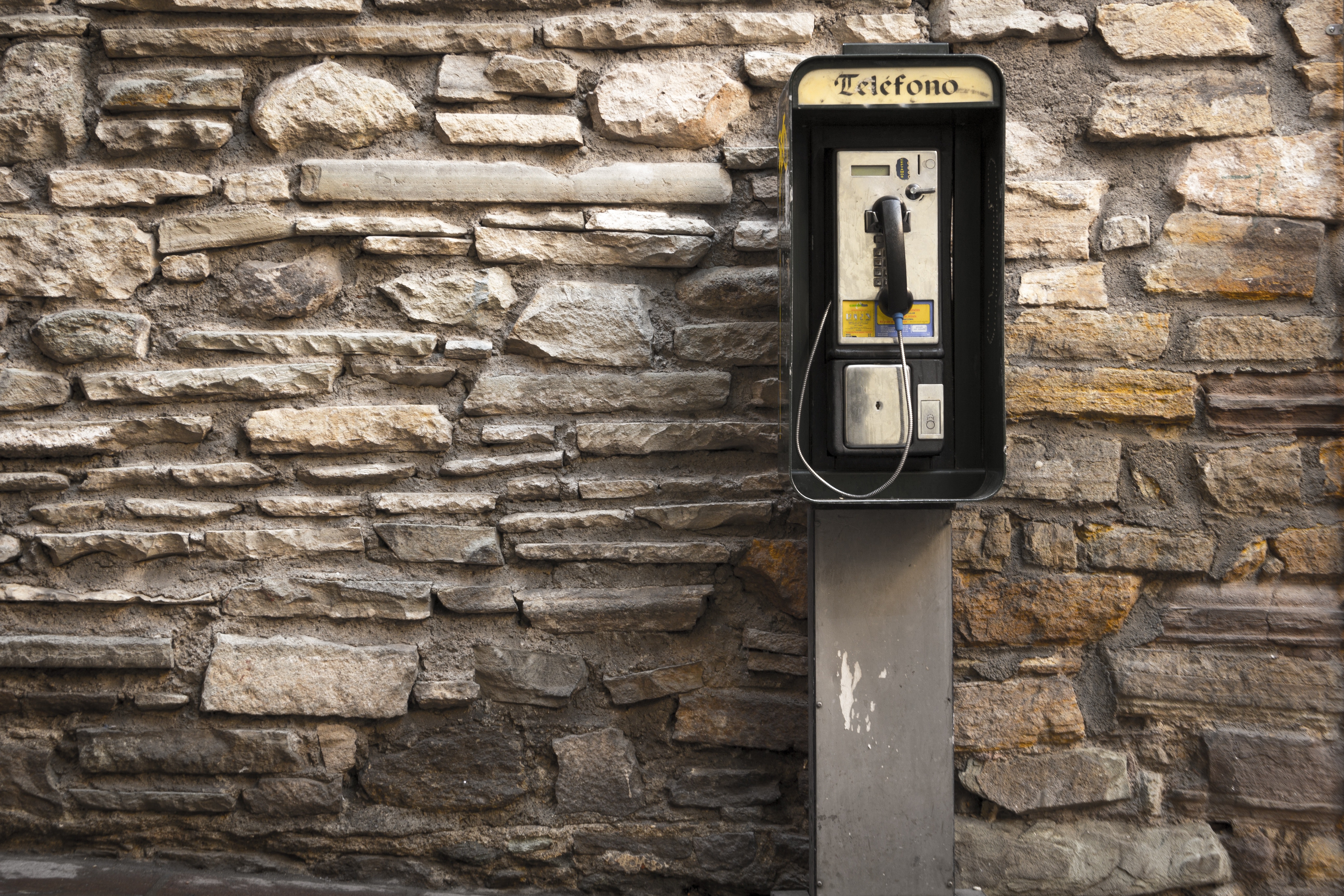 Gray and black telephone booth standing near gray stone wall at daytime photo