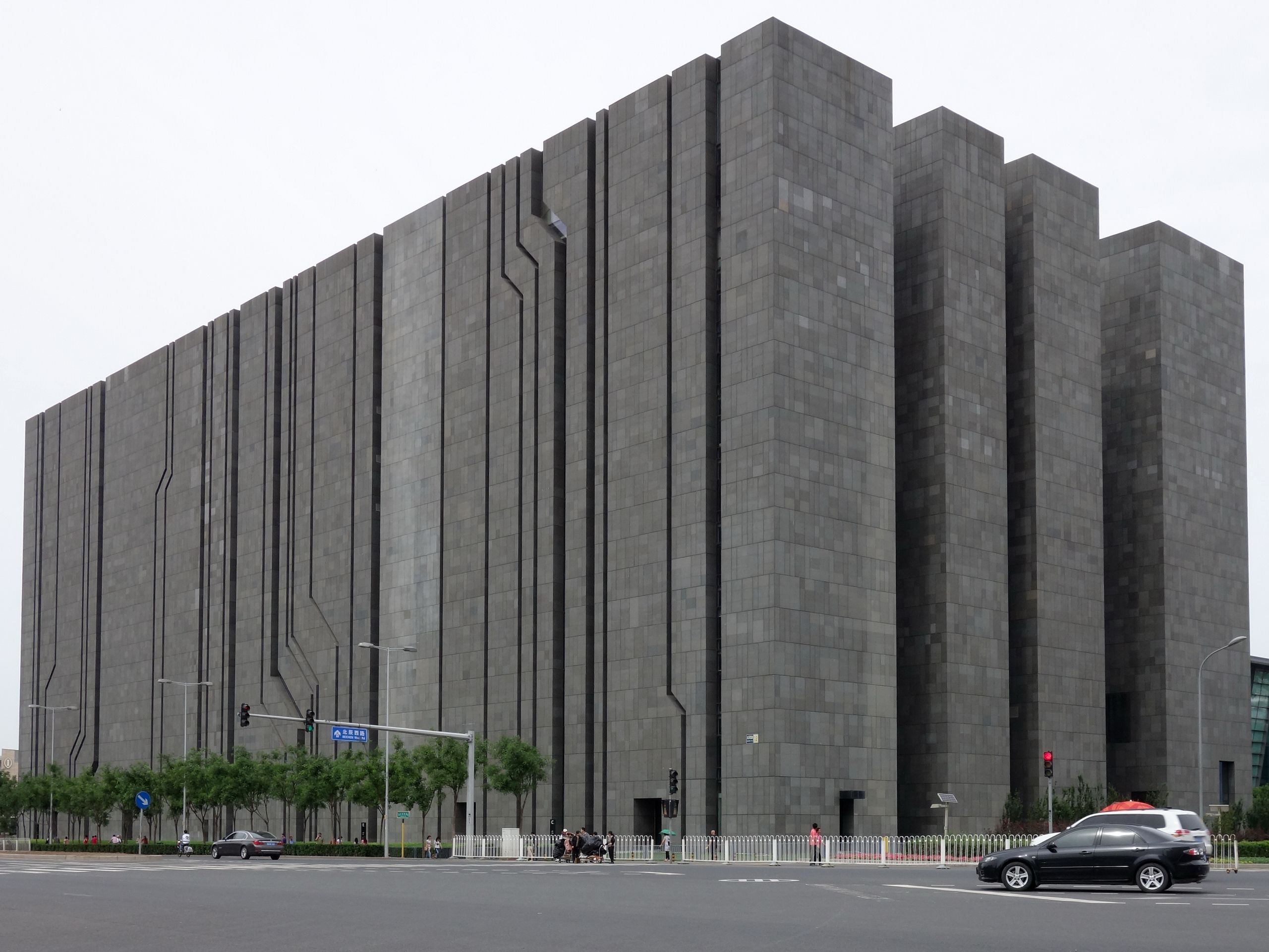 A dark gray block-like building towering over an intersection, with ...