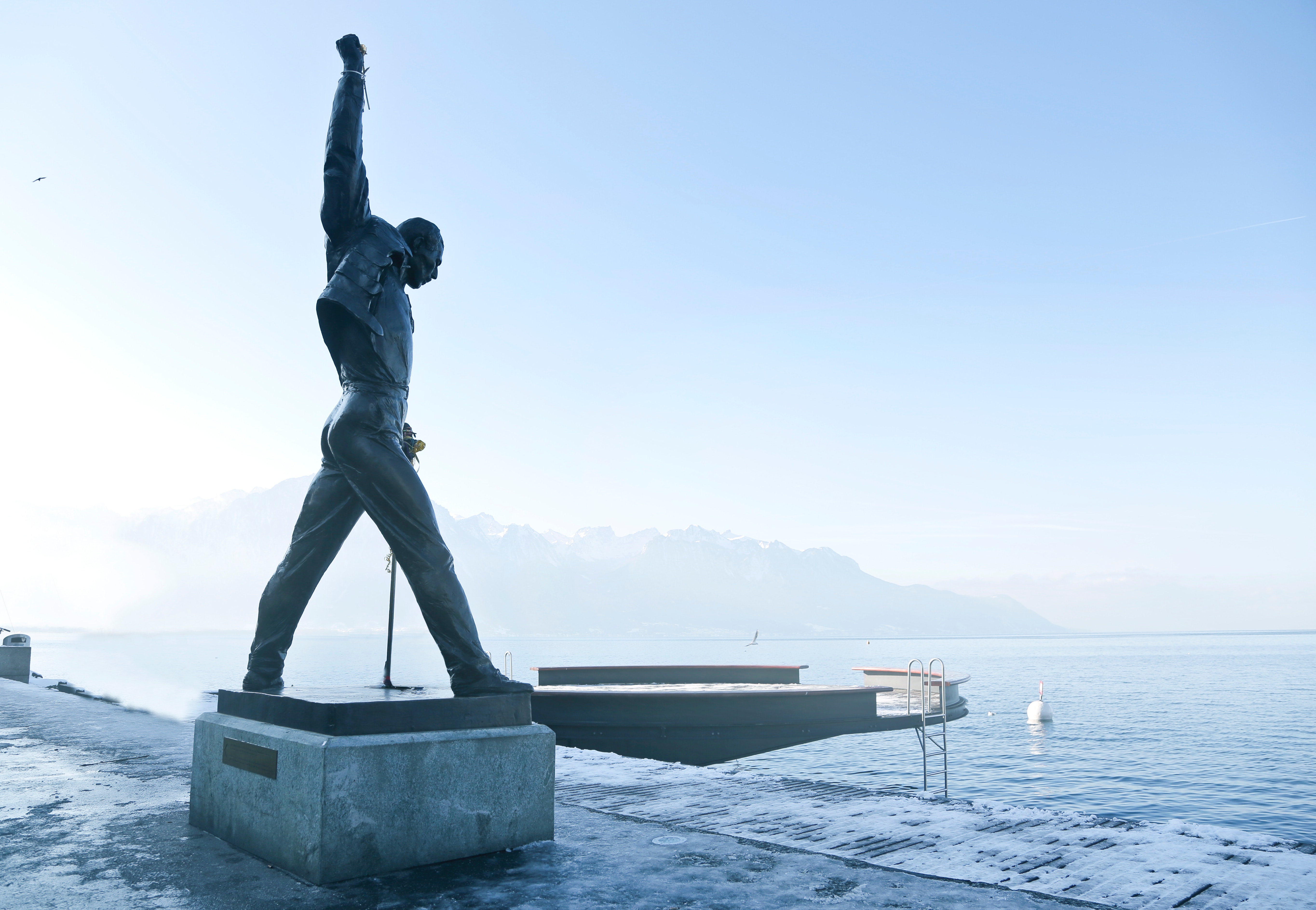Gray metal statue of man raising hand near dock photo
