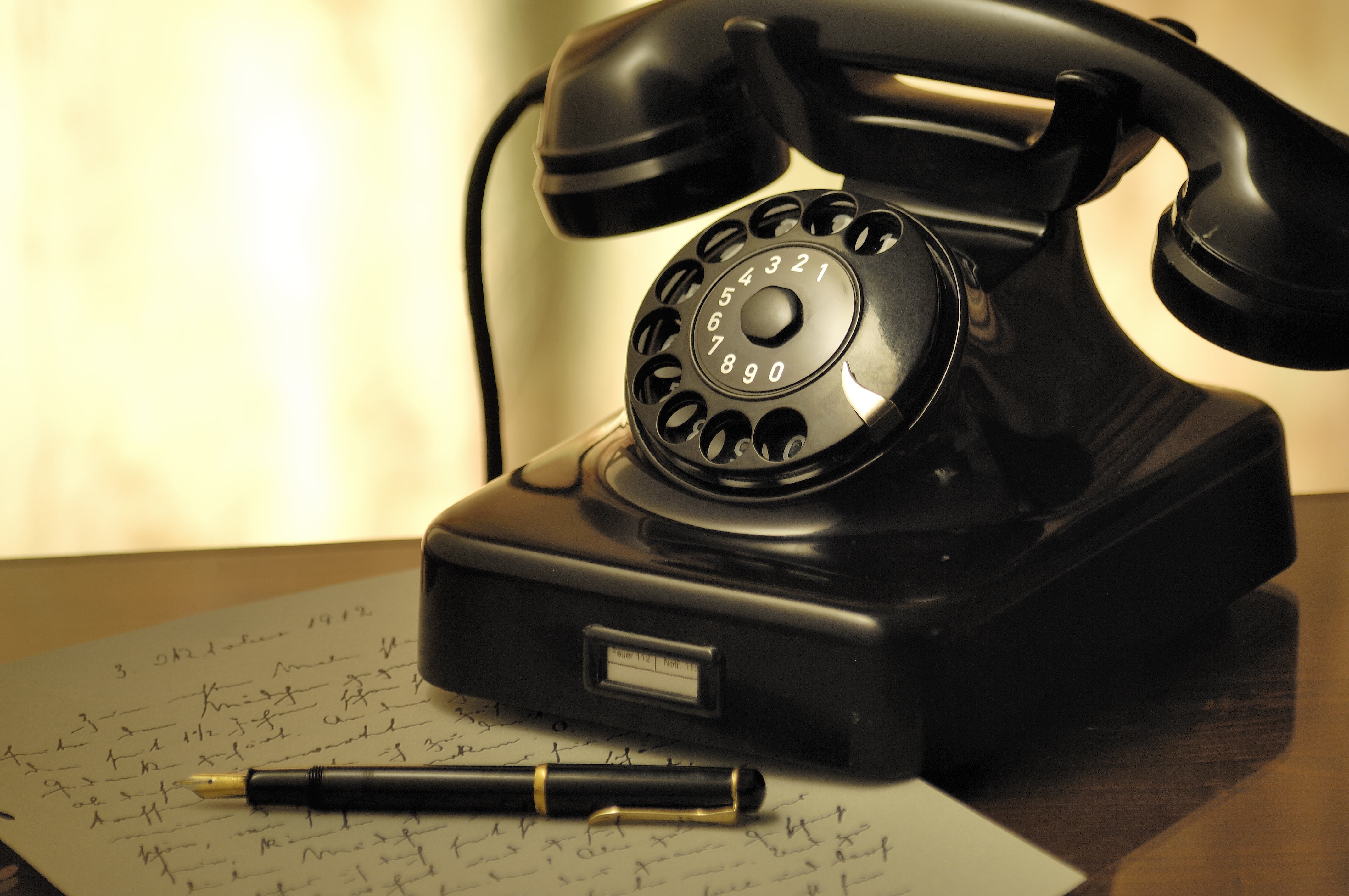 Black rotary dial telephone beside black sign pen with gray paper on ...