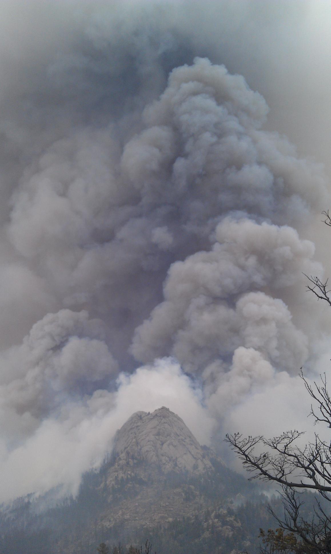Forest Service - Dark gray smoke billows above a rocky mountain peak.