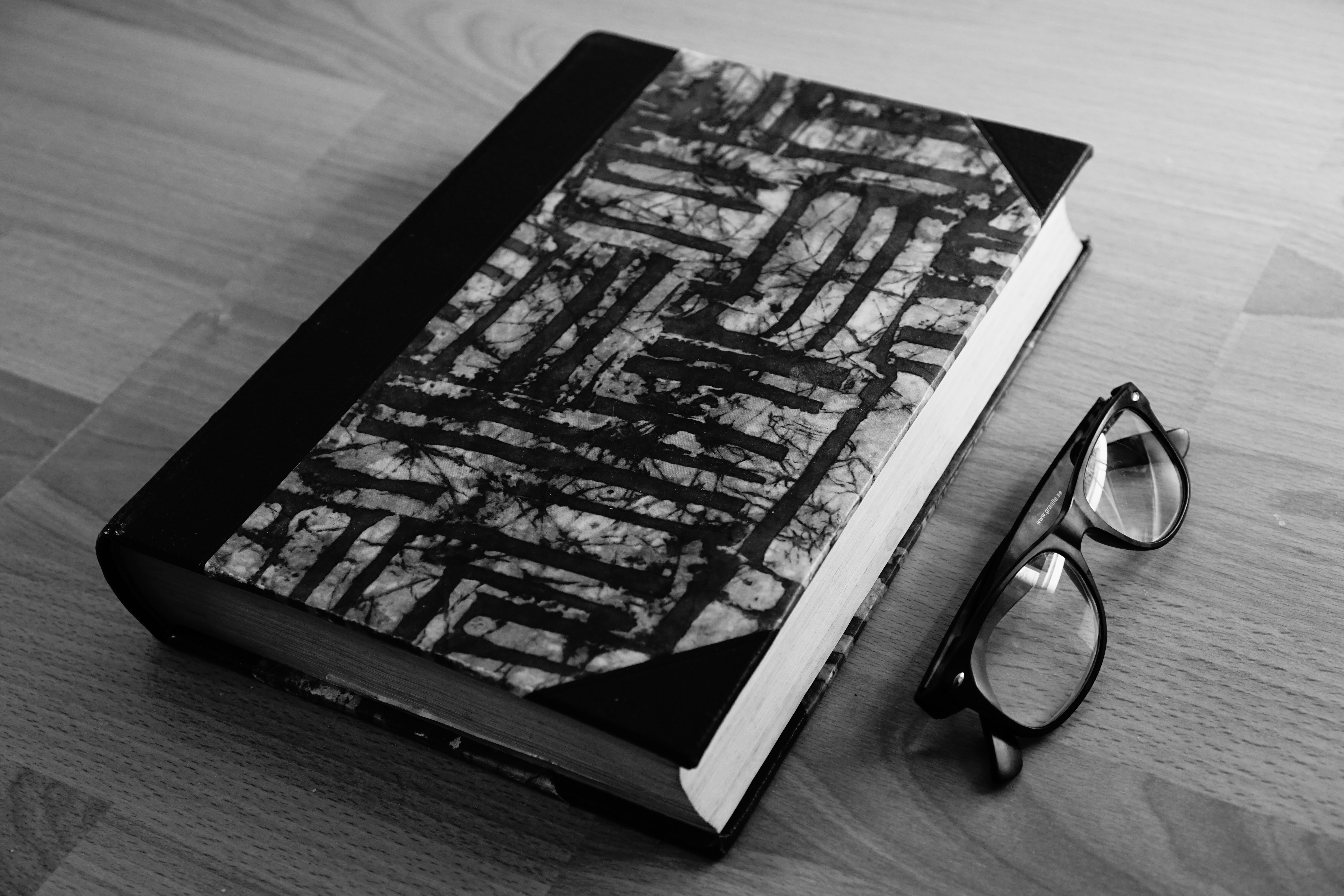 Grayscale photo of eyeglasses near thickbound book