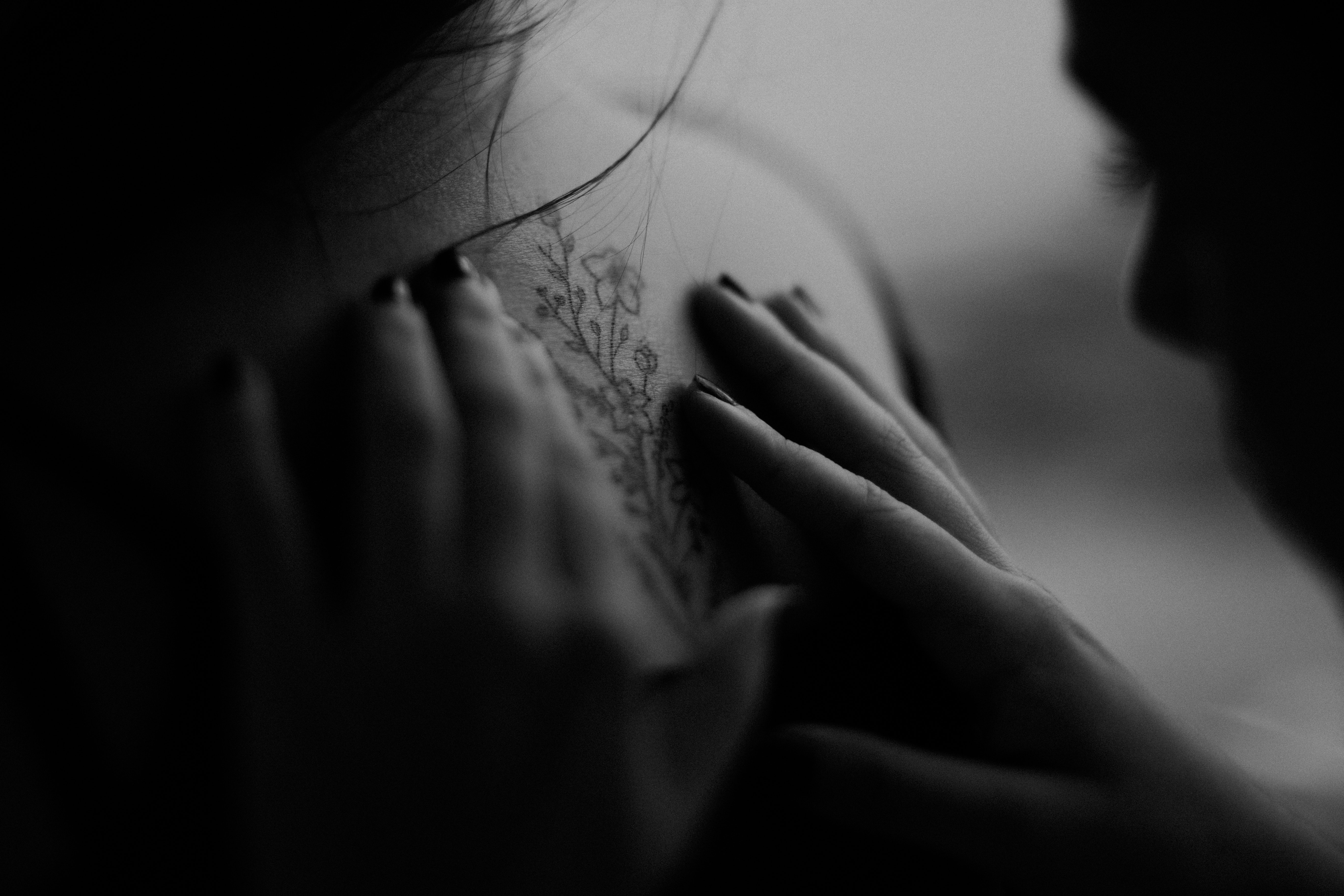 Grayscale photo of man looking at woman's back flower tattoo