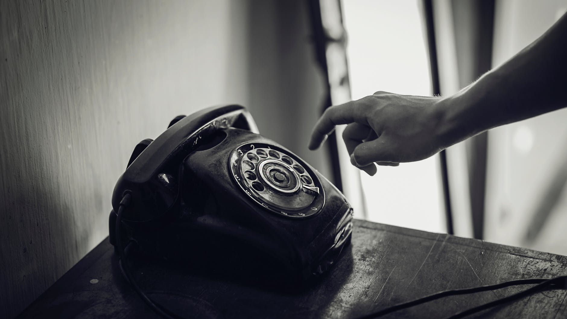 Grayscale photo of rotary telephone beside person hand