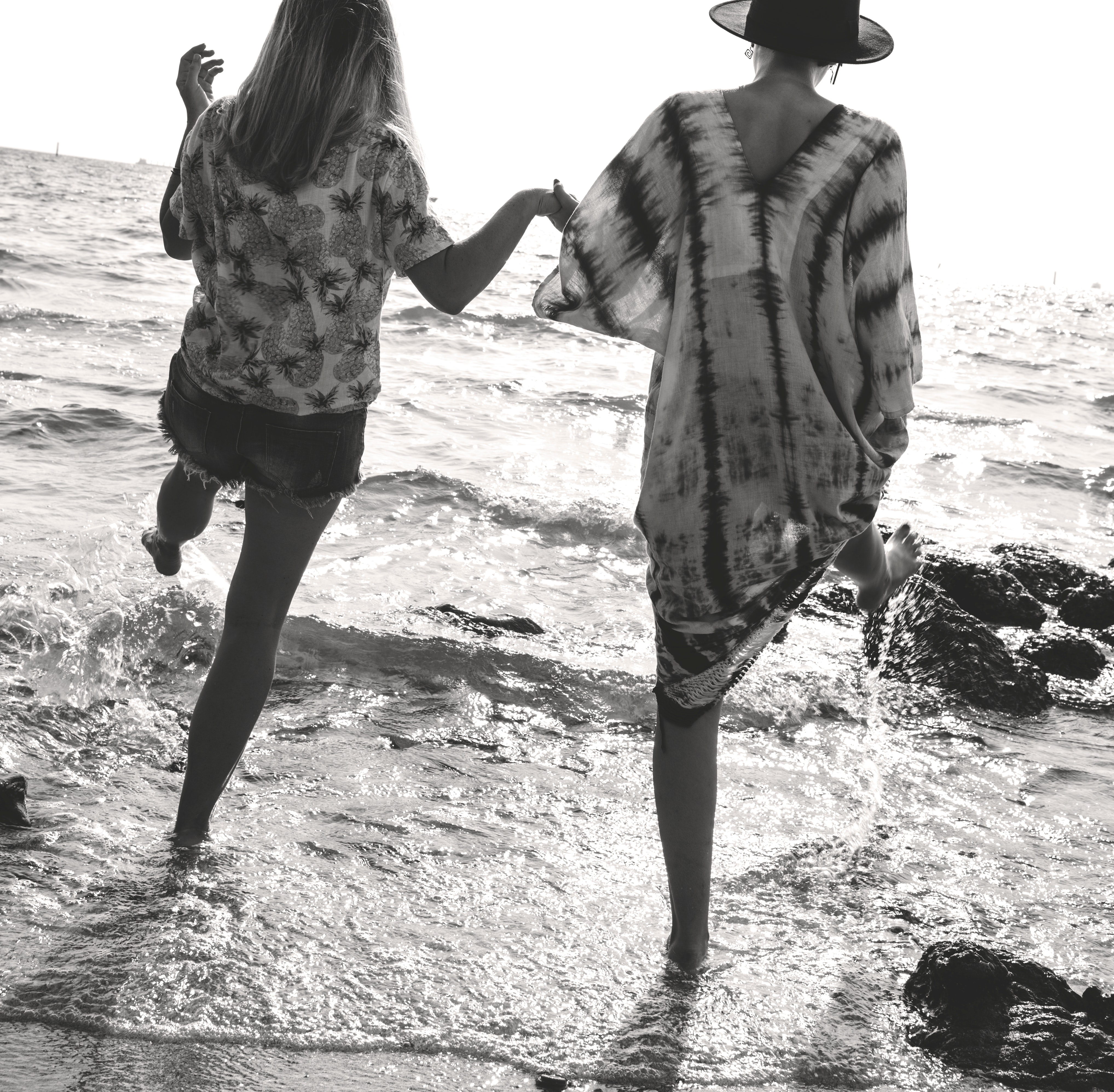 Grayscale photograph of 2 women holding hands while walking on sea shore