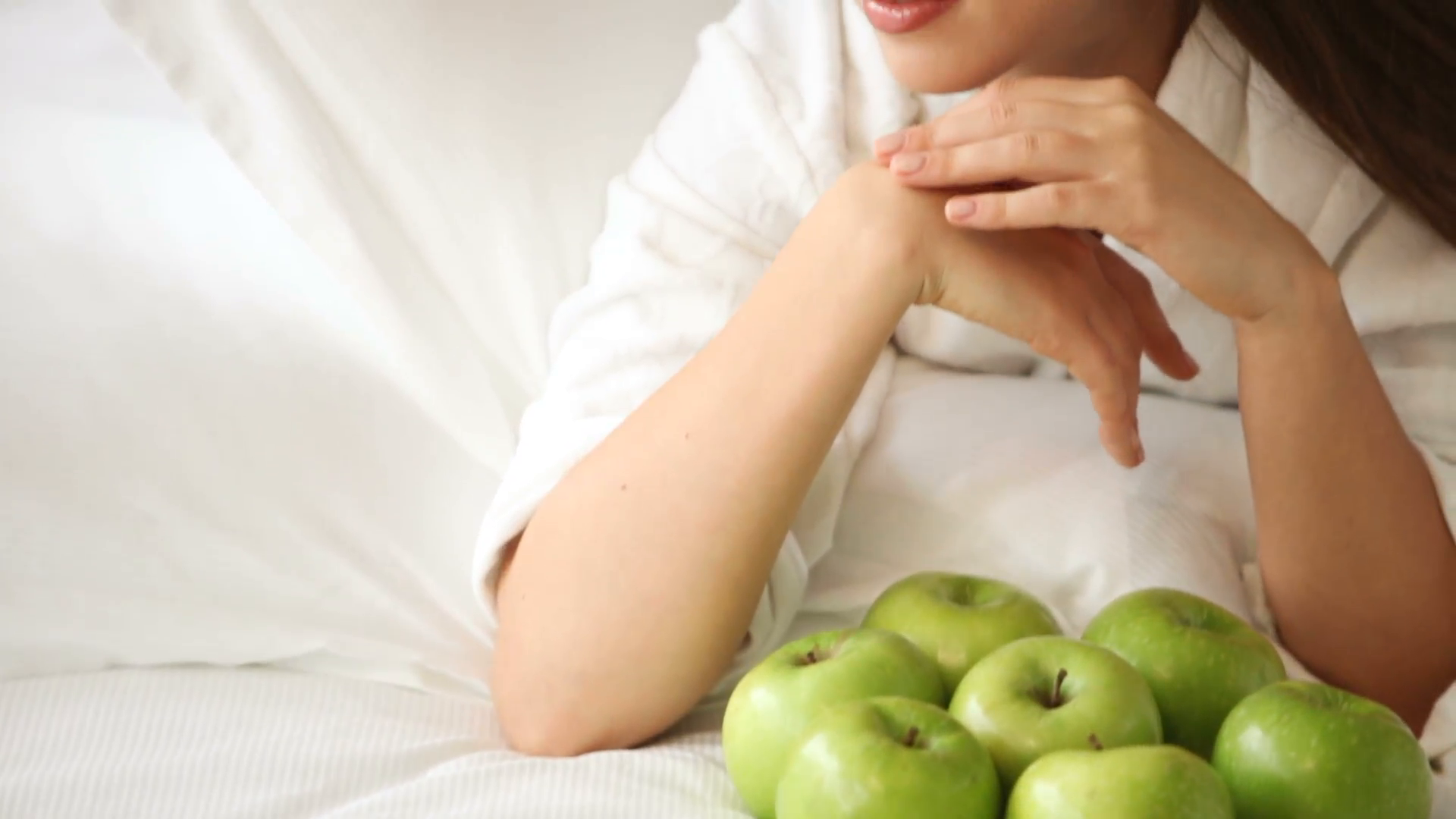 Charming young woman lying on bed with lot of green apples looking ...