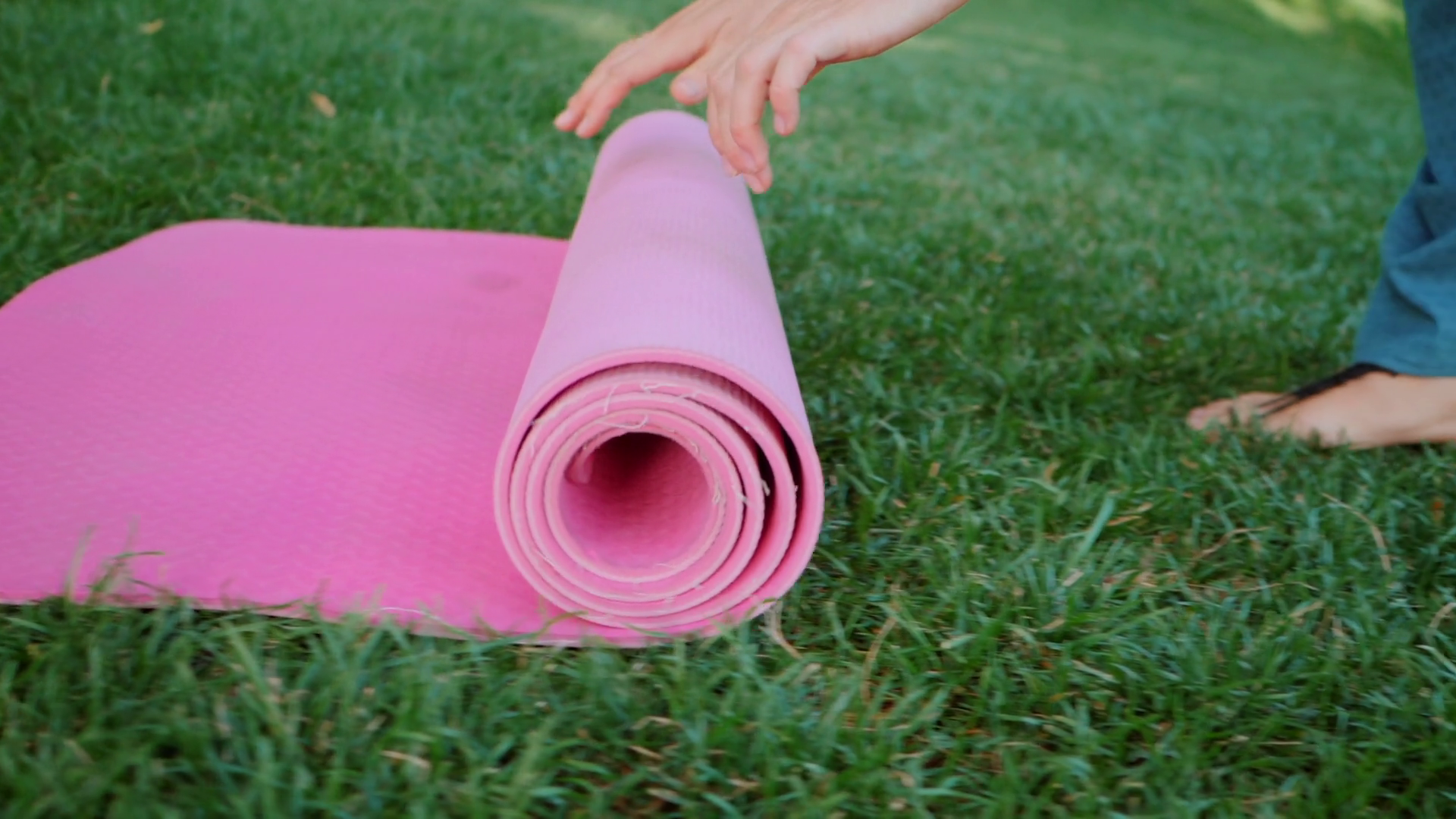 Young woman doing yoga exercise - opening her pink yoga mat on green ...