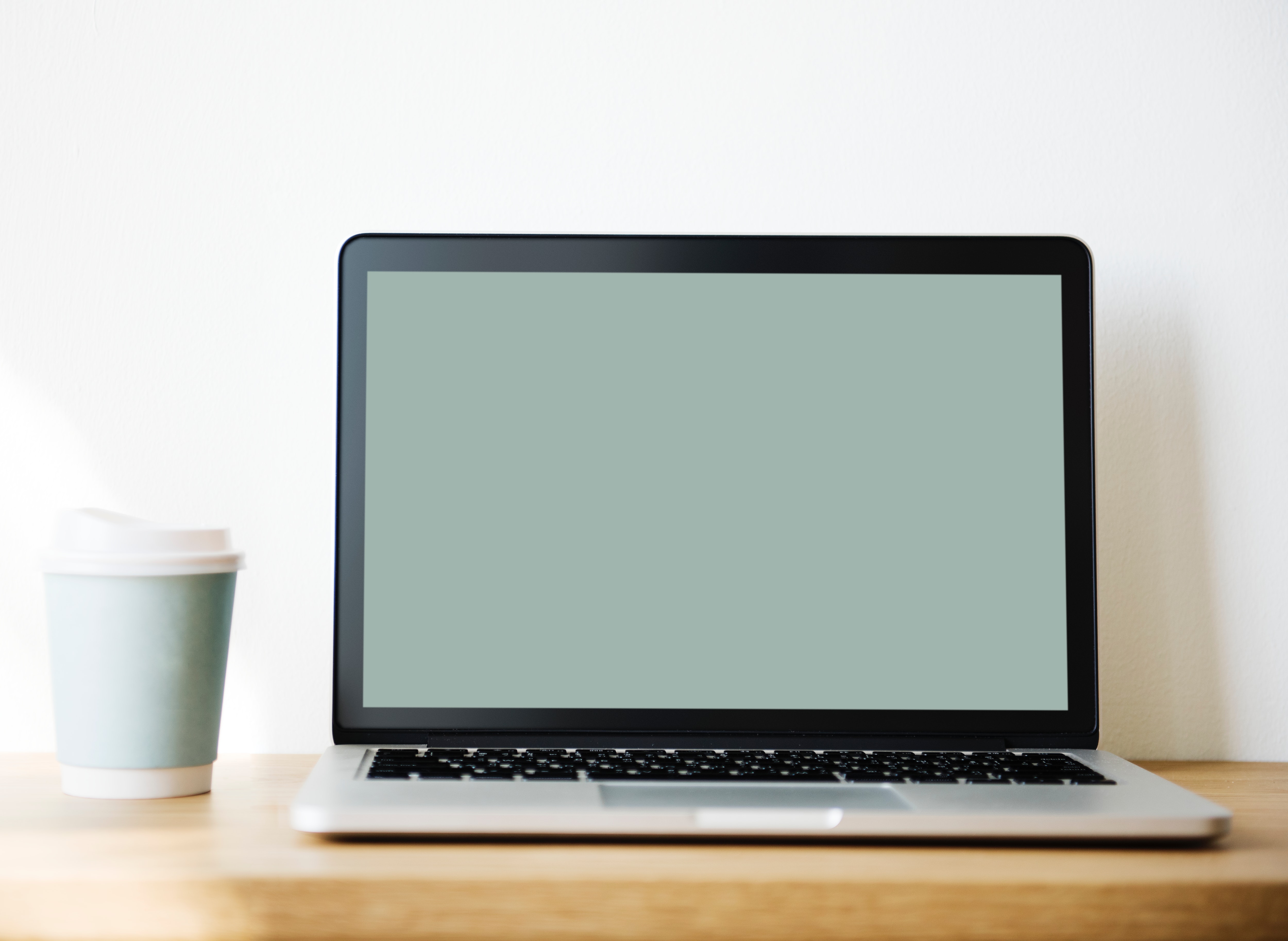 Grey and black laptop beside white and teal coffee cup photo
