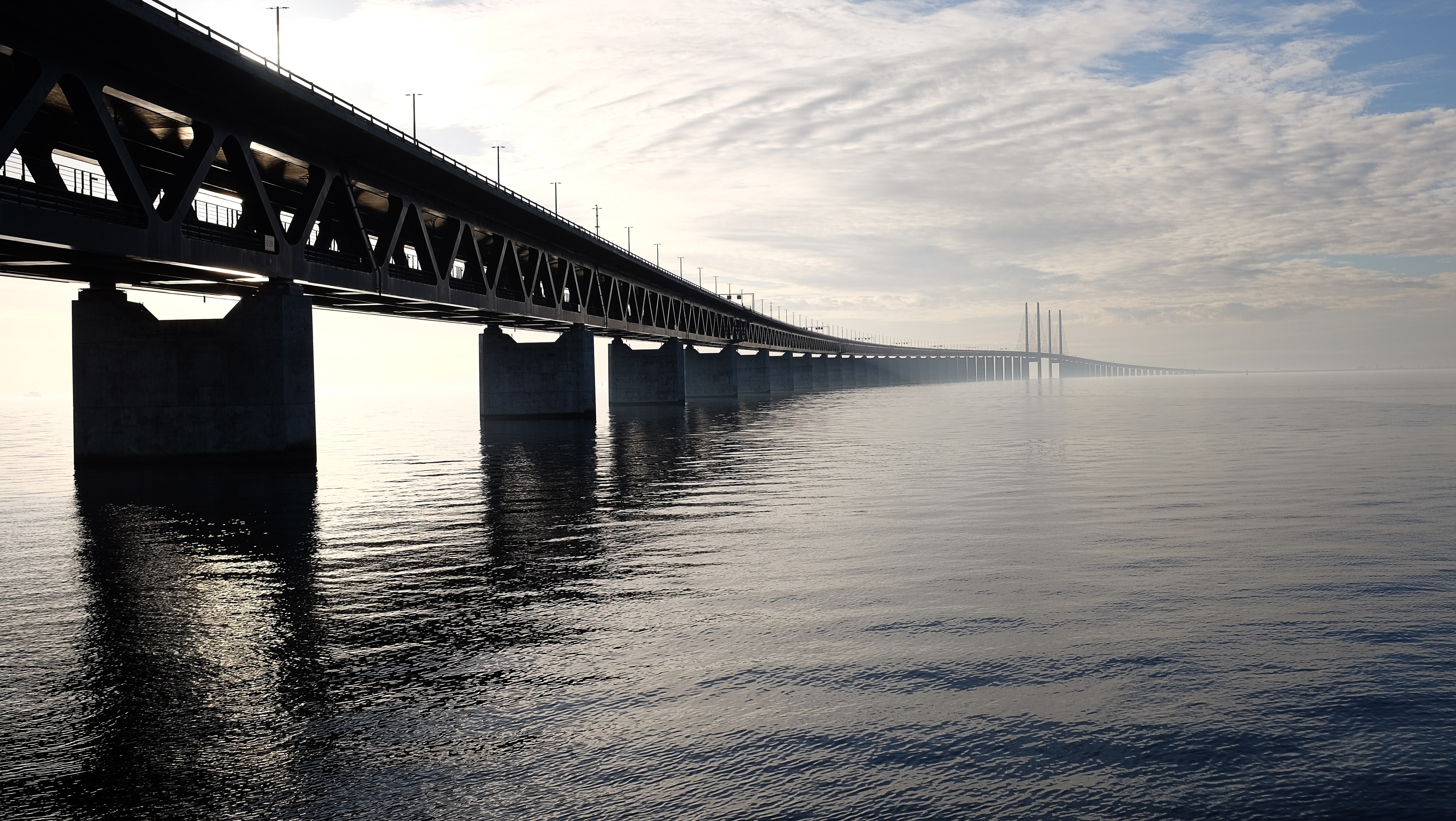 Grey concrete bridge on body of water under blue and white sky during daytime photo
