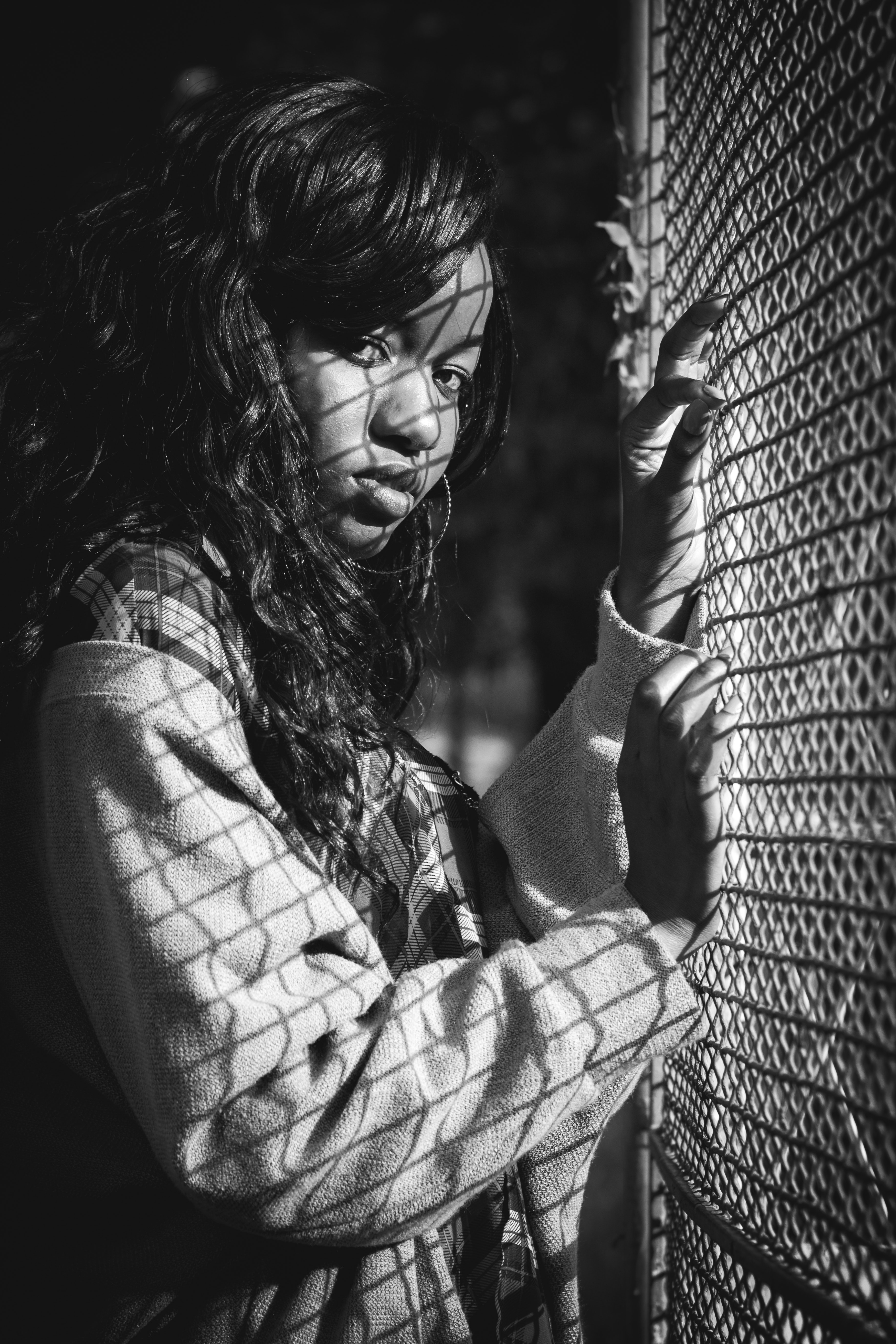 Grey scale photography of woman standing against mesh grill