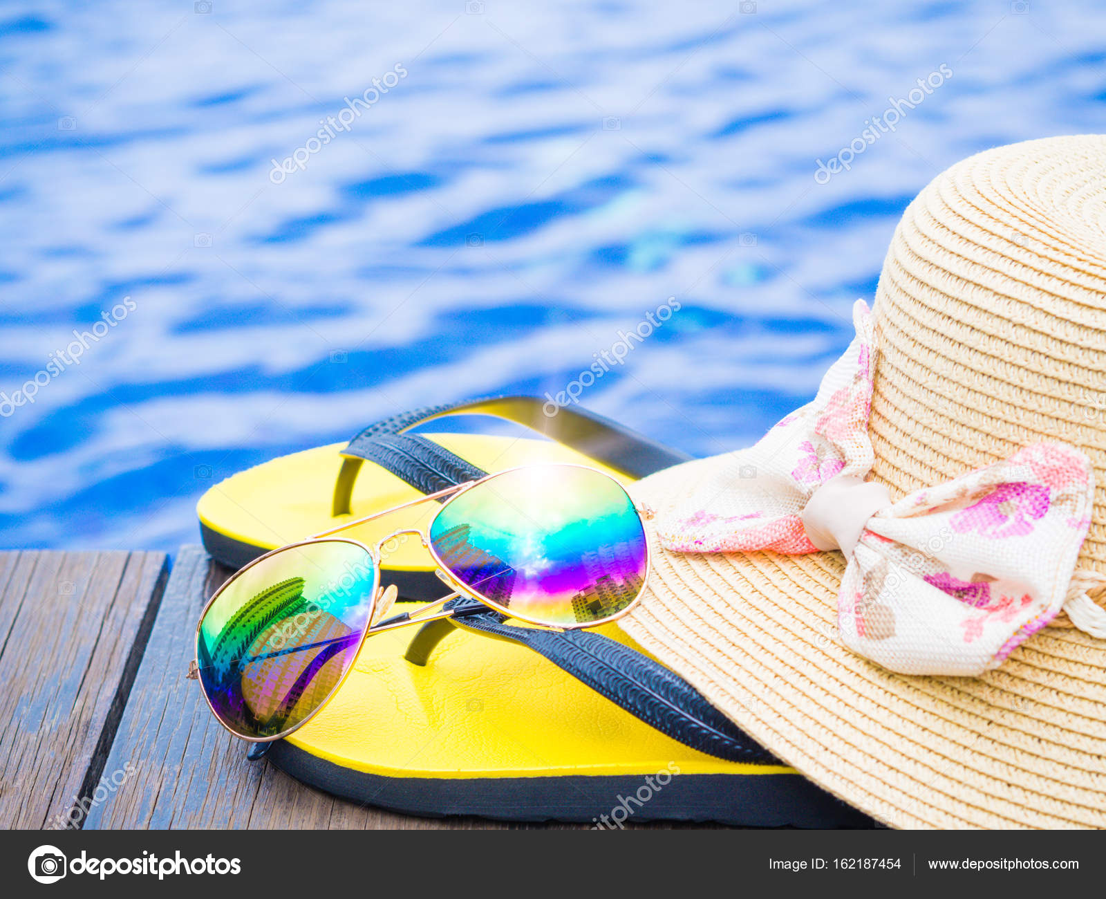 Summer hat with sunglasses and flip flops by the swimming pool ...