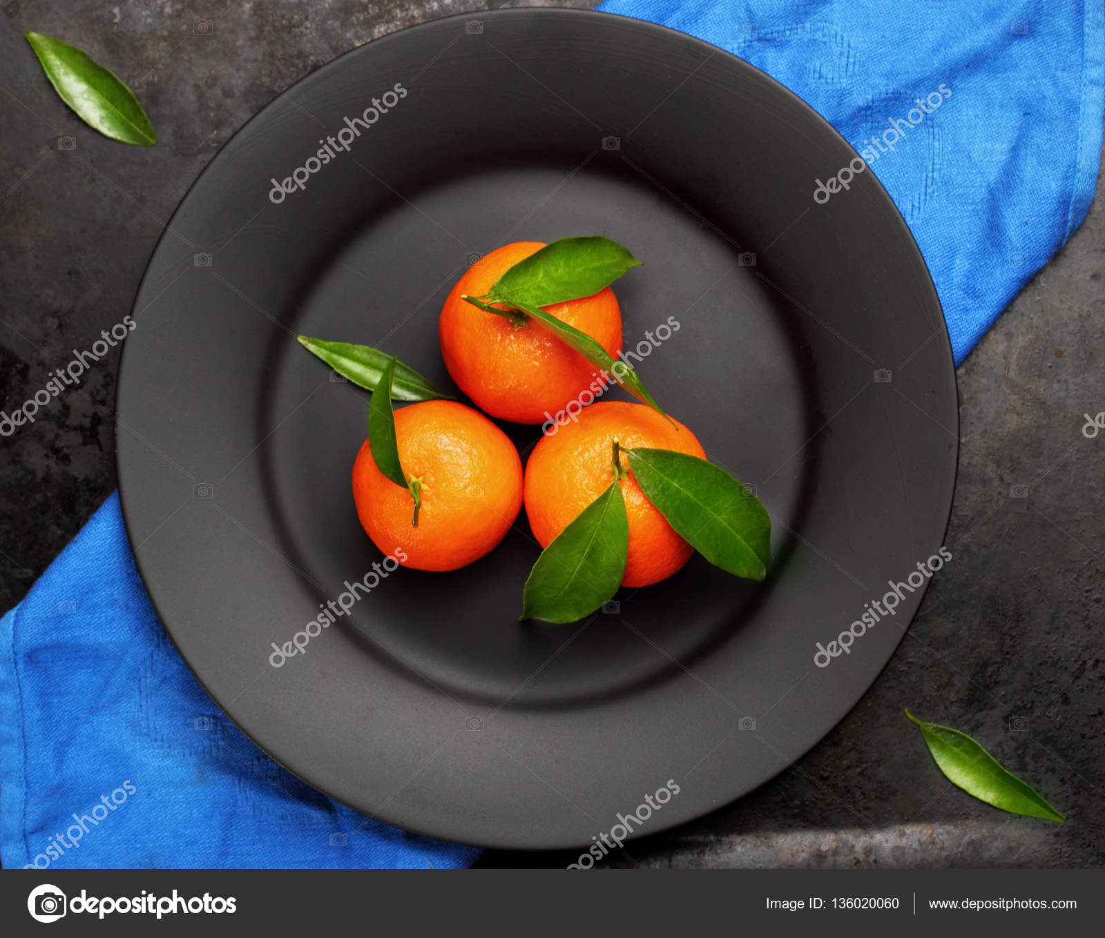 Ripe orange tangerines with green leaves on black ,matt plate , top ...
