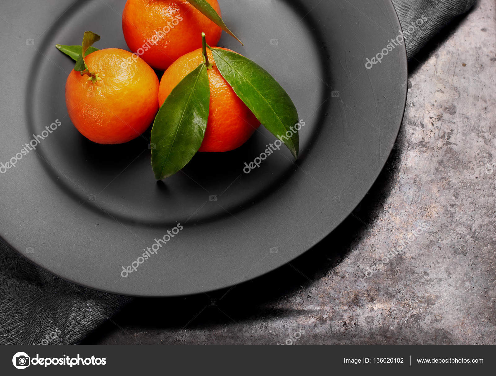 Ripe orange tangerines with green leaves on black ,matt plate , top ...