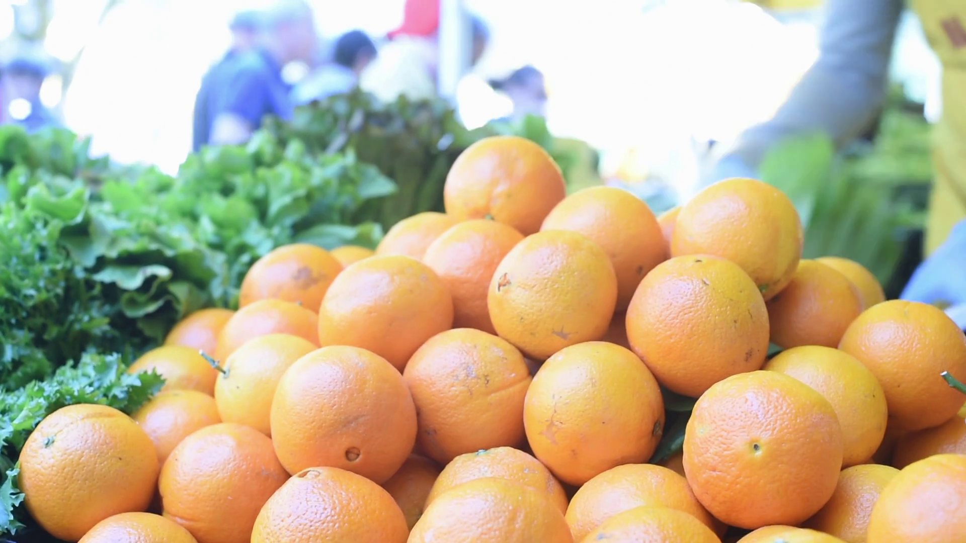 Orange fruits heap on a market stall, people in background around ...