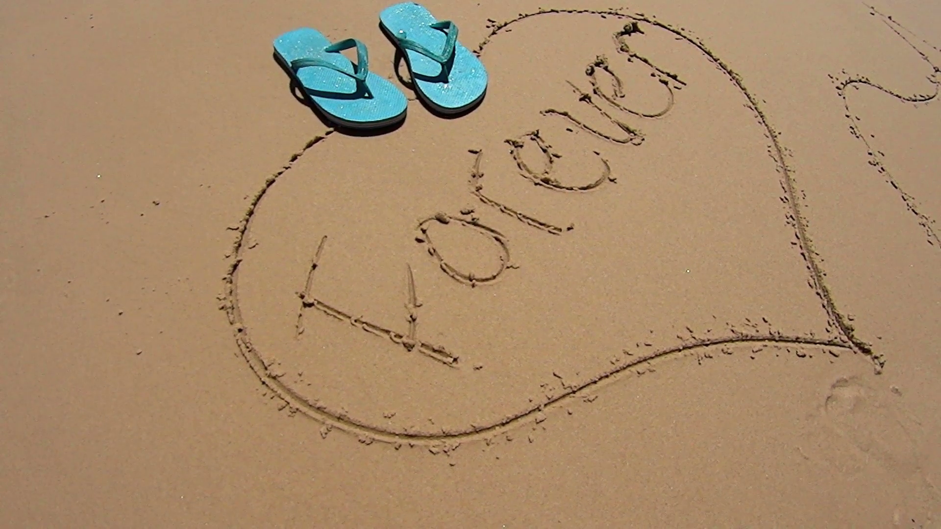 Pair of flip flops dropped on a love heart drawn in the sand on a ...