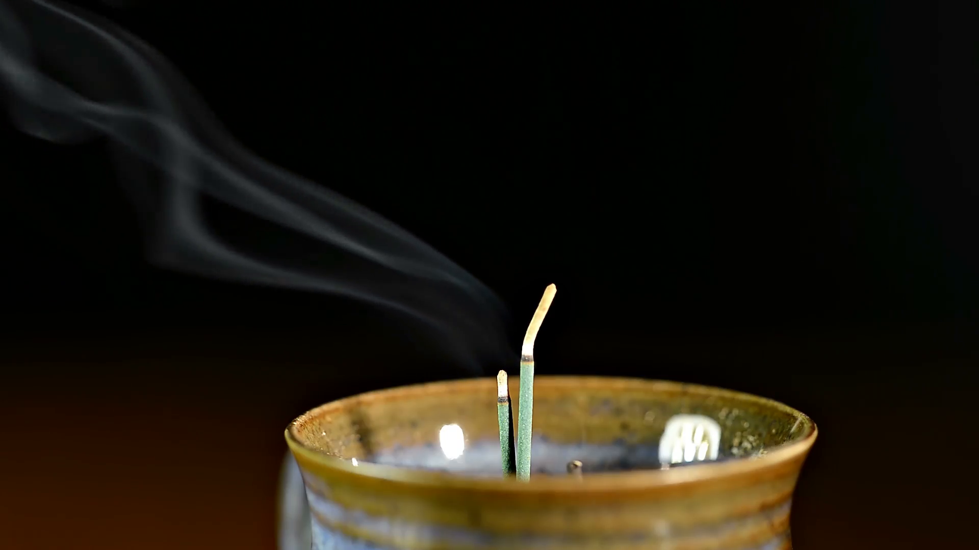 Green incense sticks burning in golden pottery pot with ash falling ...