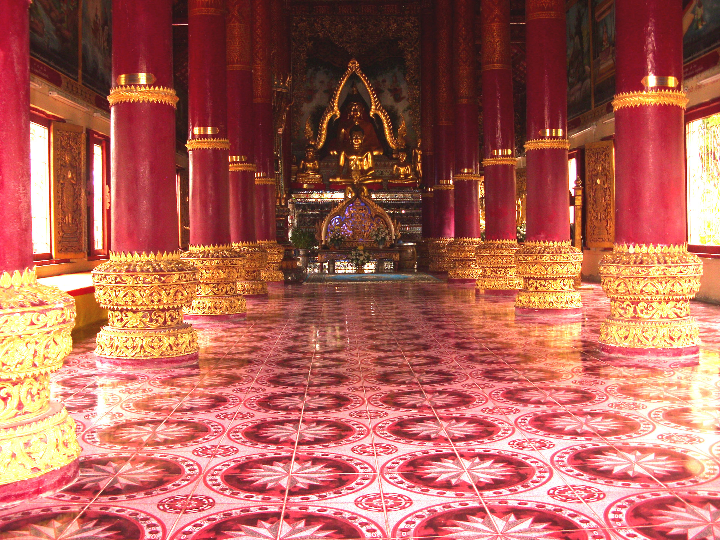  The image shows a large open room with red pillars and a golden Buddha statue at the end of the room.