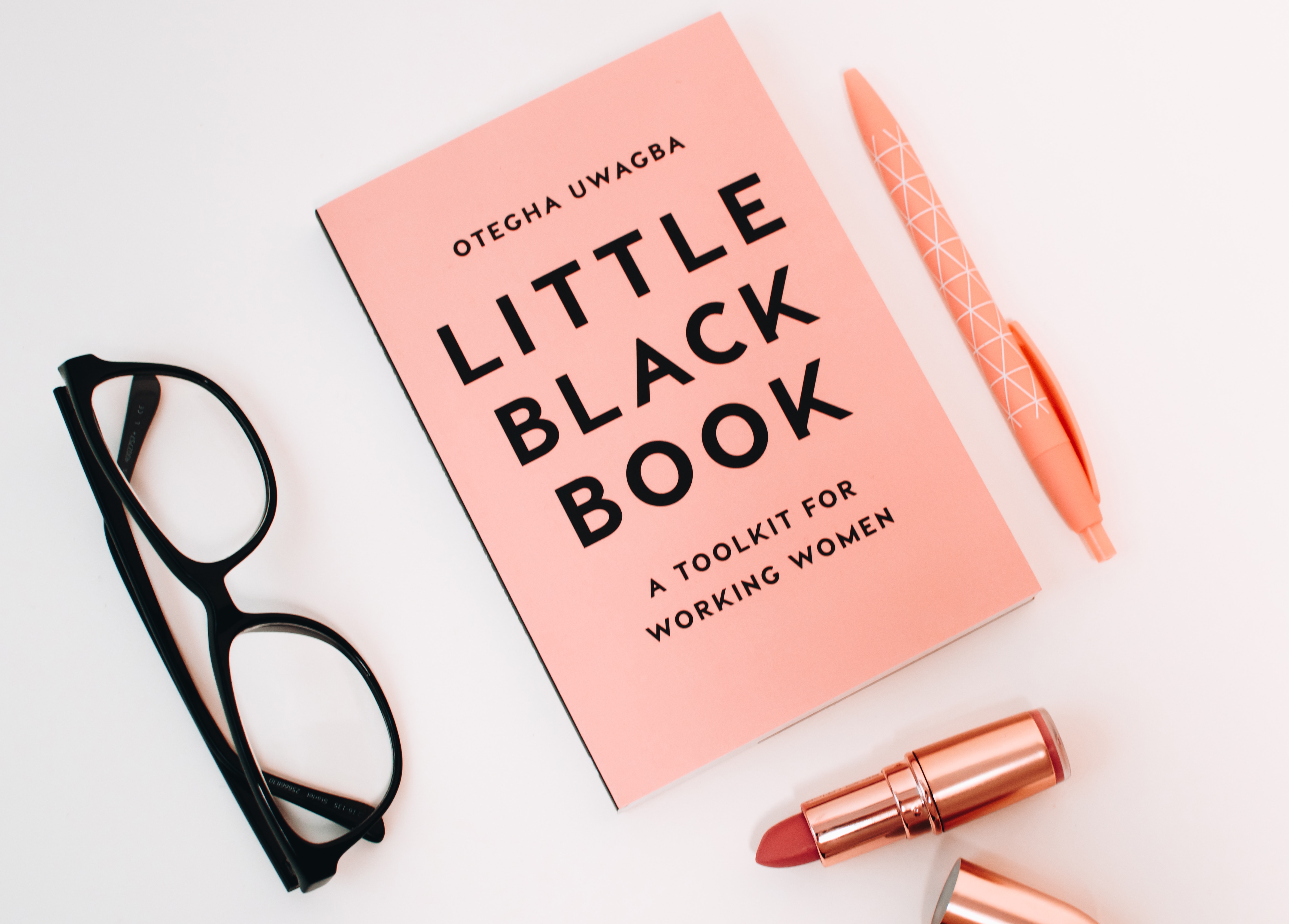 Little black book surrounded with pink click pen, red lipstick, and black wayfarer eyeglasses photo