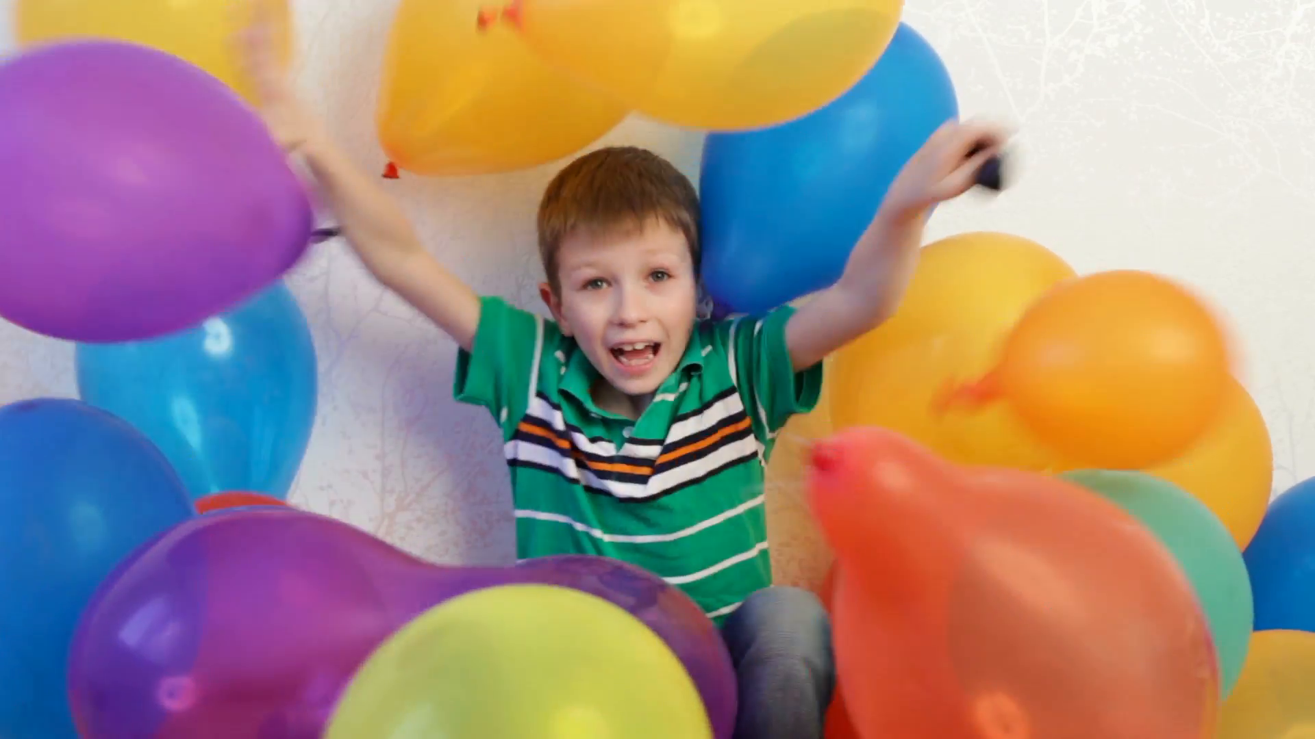 A little boy playing at home with balloons, hiding in it and then ...