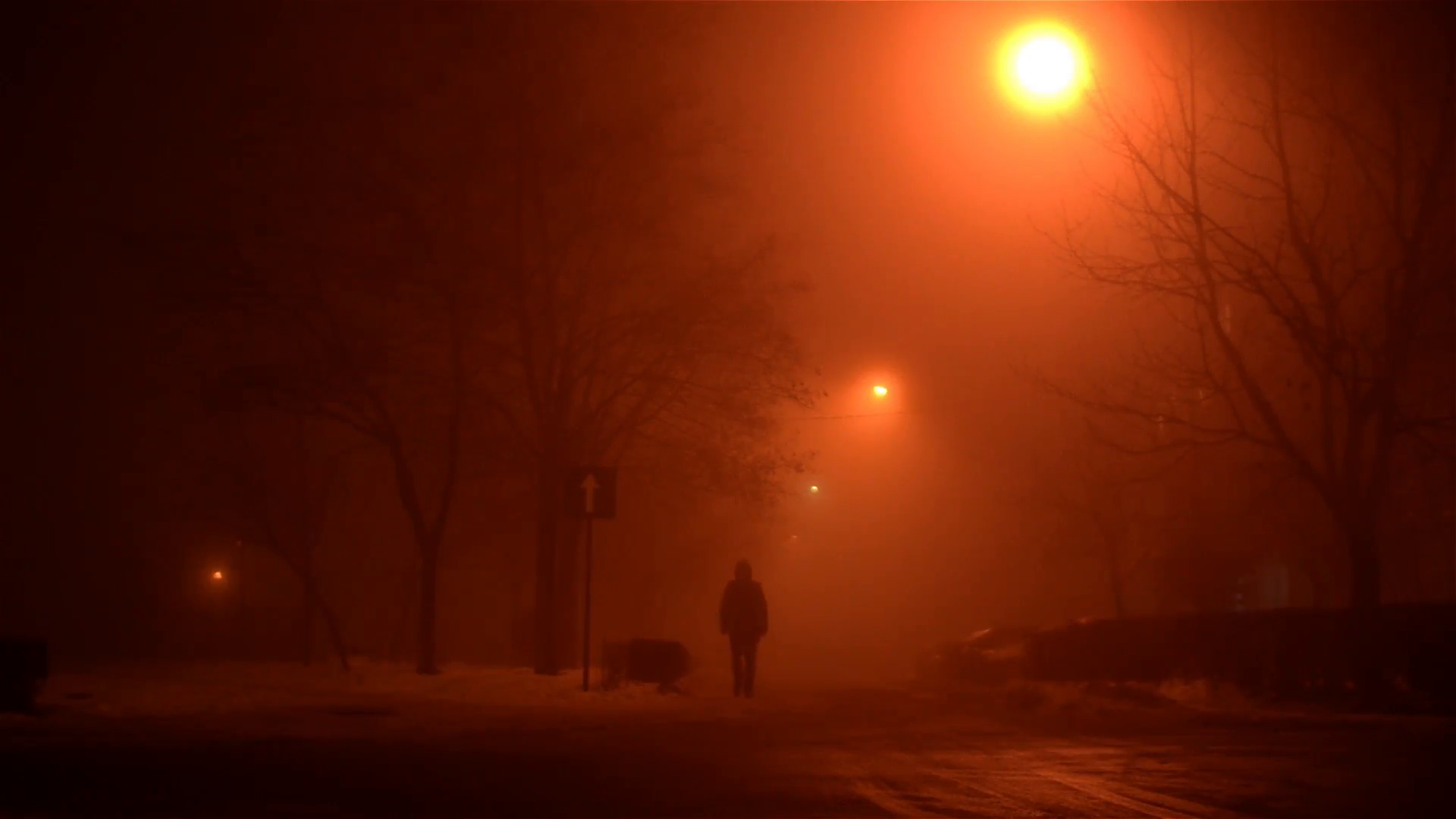 Lone person walks on a snowy street in an orange haze night, in a ...