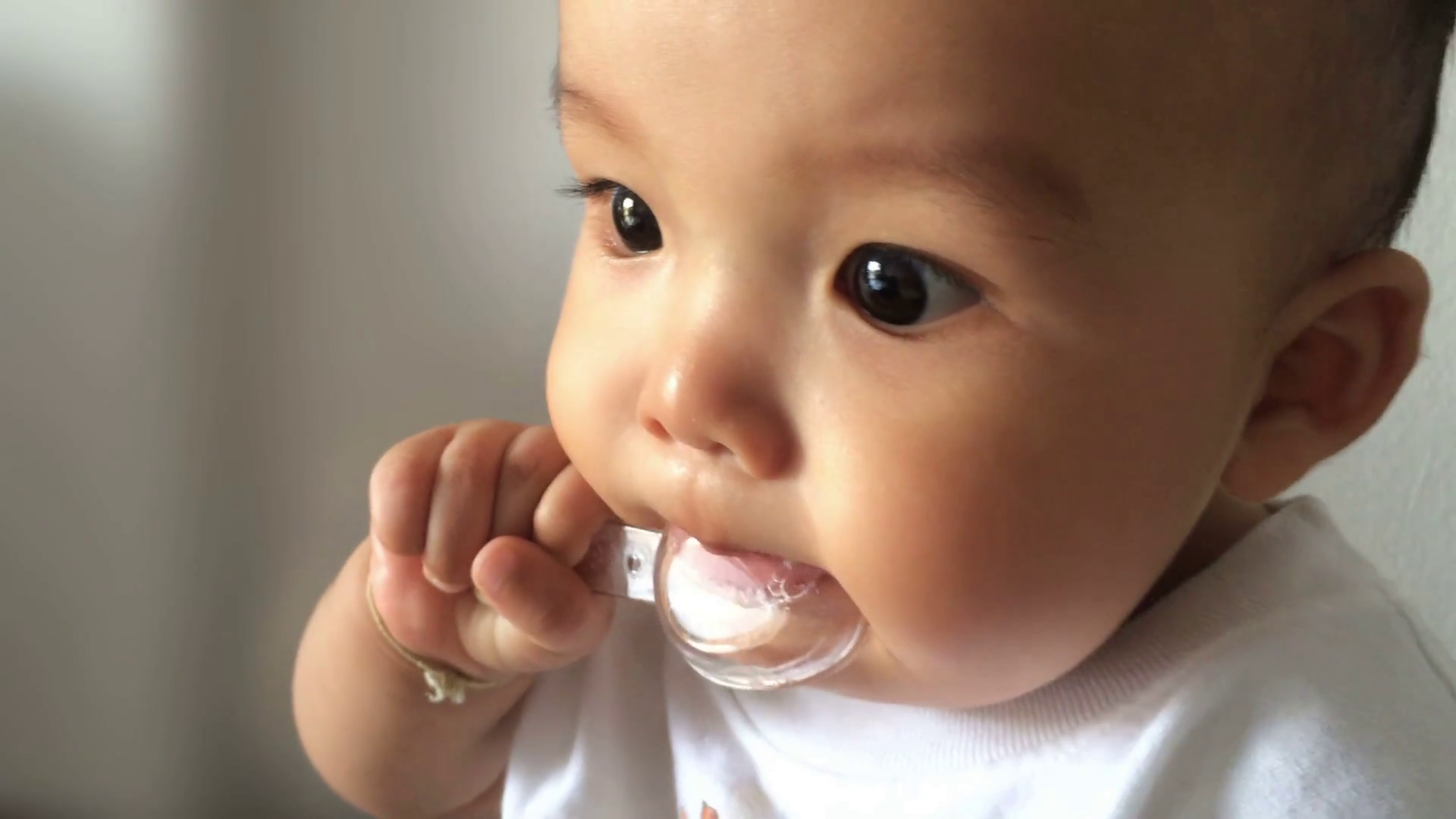 Baby holding a transparent spoon in the mouth and looking outside ...