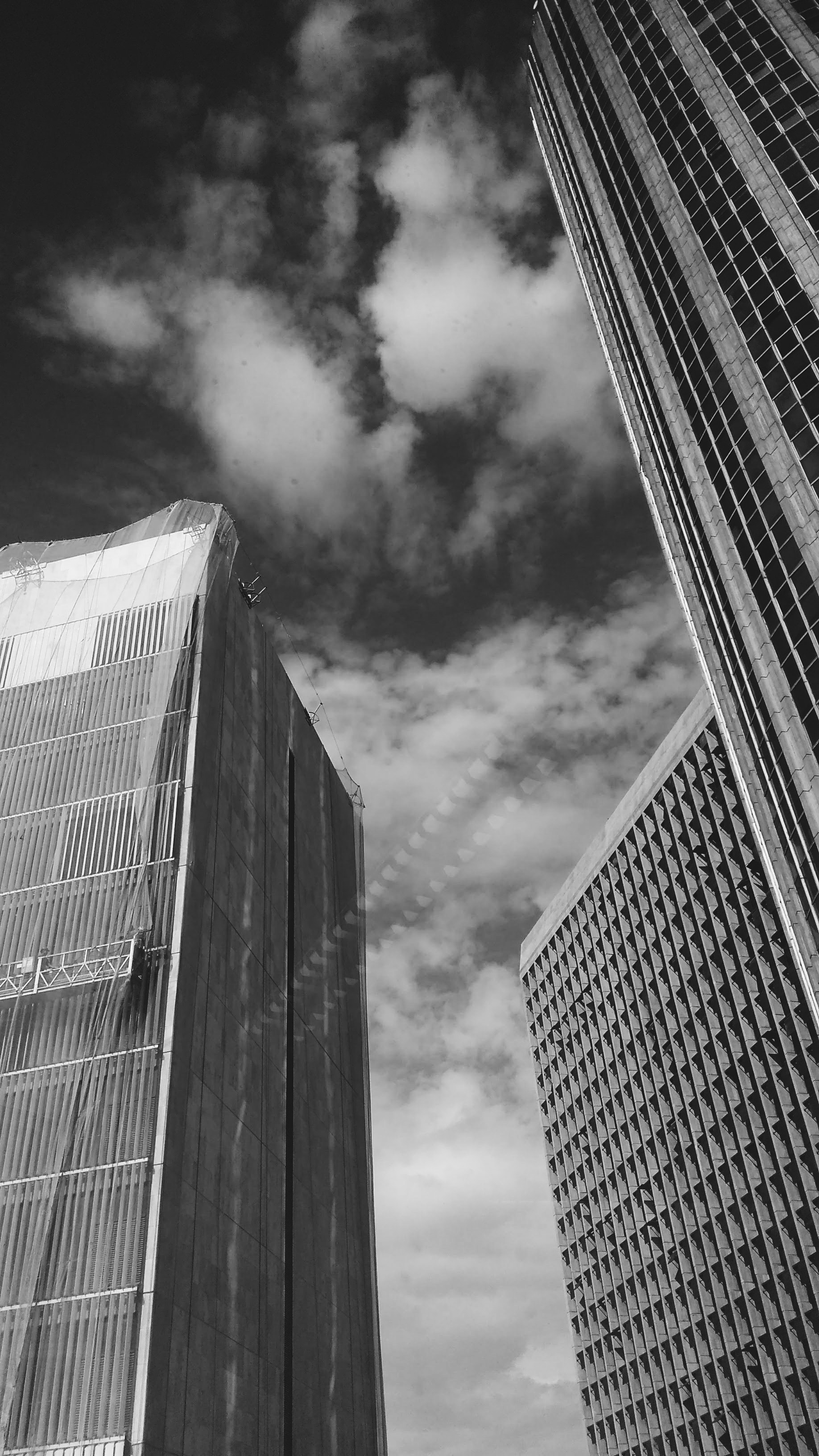 Low angle grayscale photography of buildings and clouds