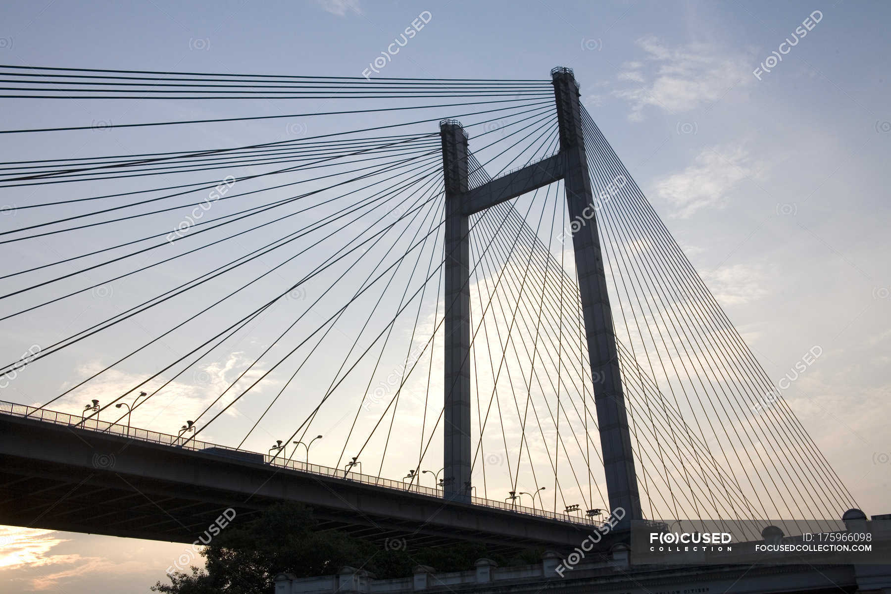 Low angle view of bridge construction with wires against cloudy sky ...
