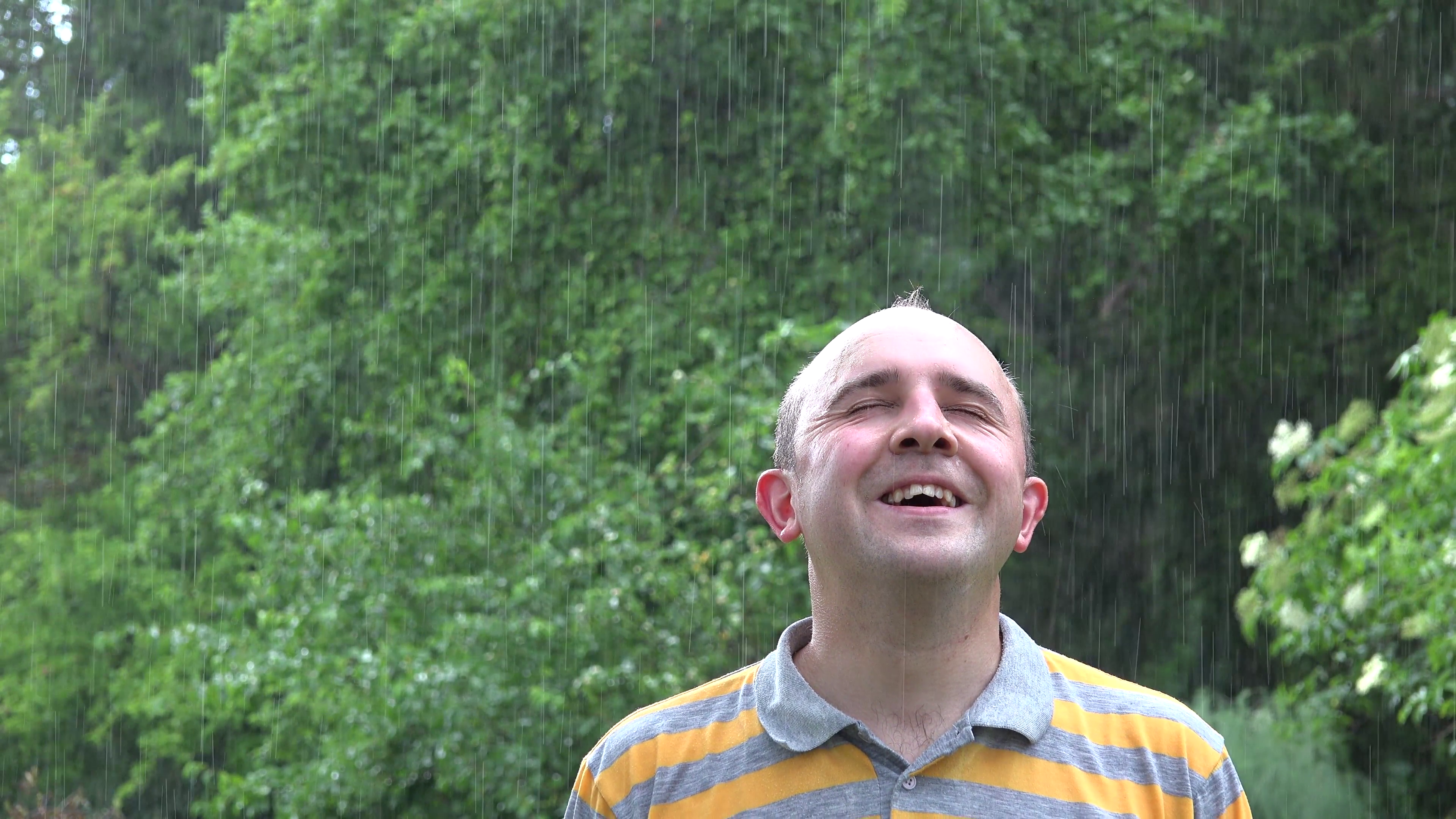 Happy wet man with hands rises up spin around under heavy rain. 4K ...