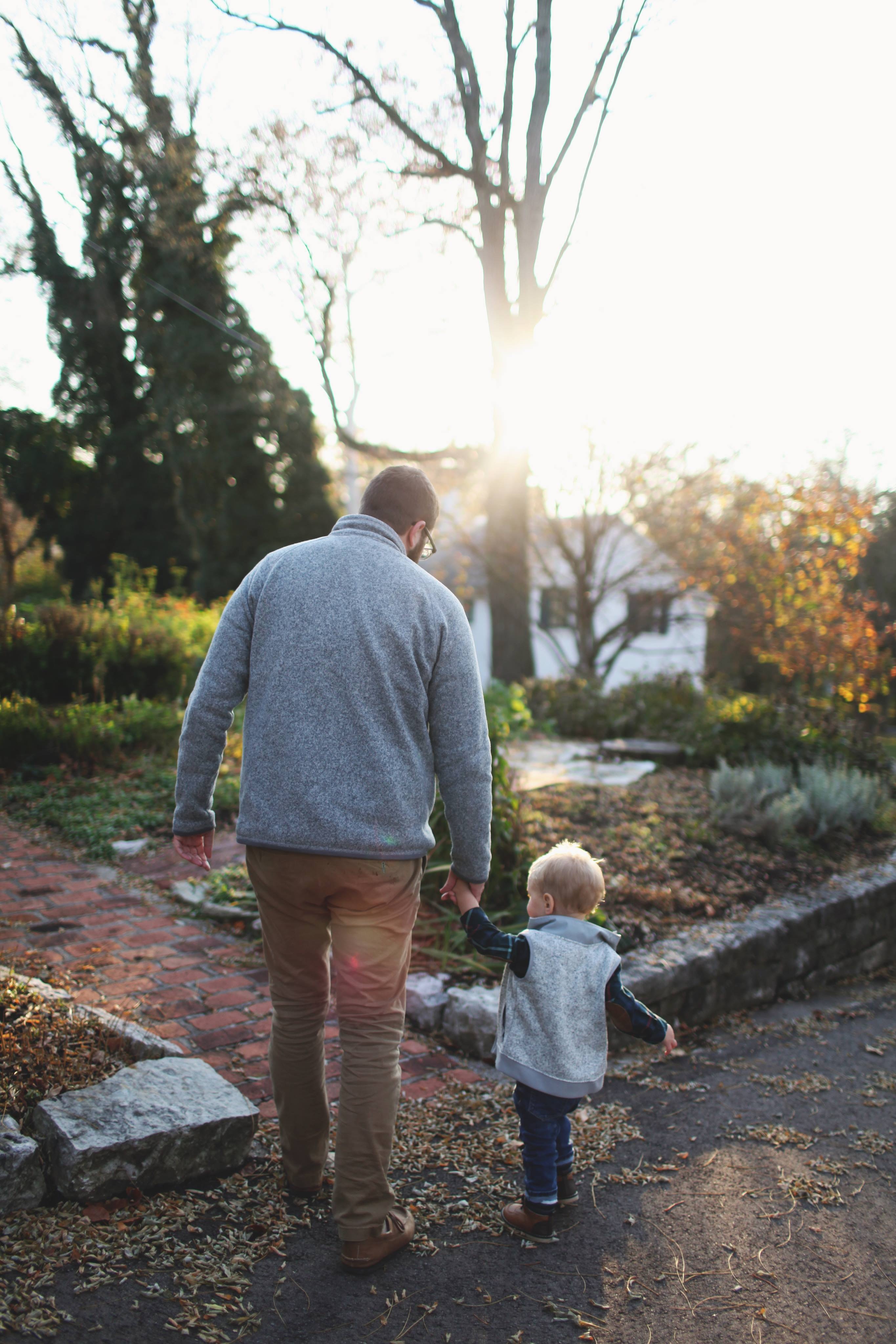 Man holding hands with baby while walking through pathway facing sunlight photo