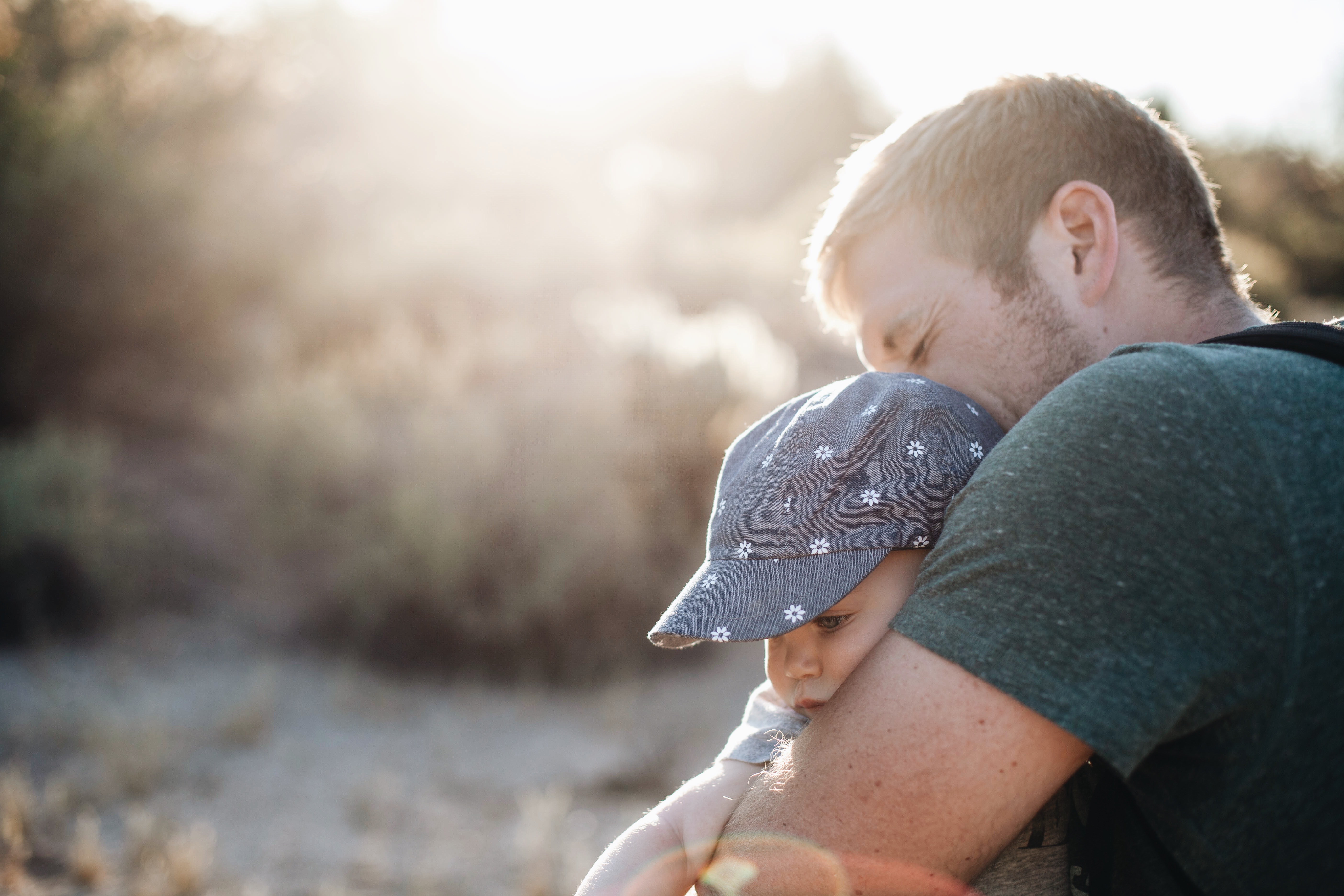 Man hugging the baby in blue floral fitted cap during daytime photo