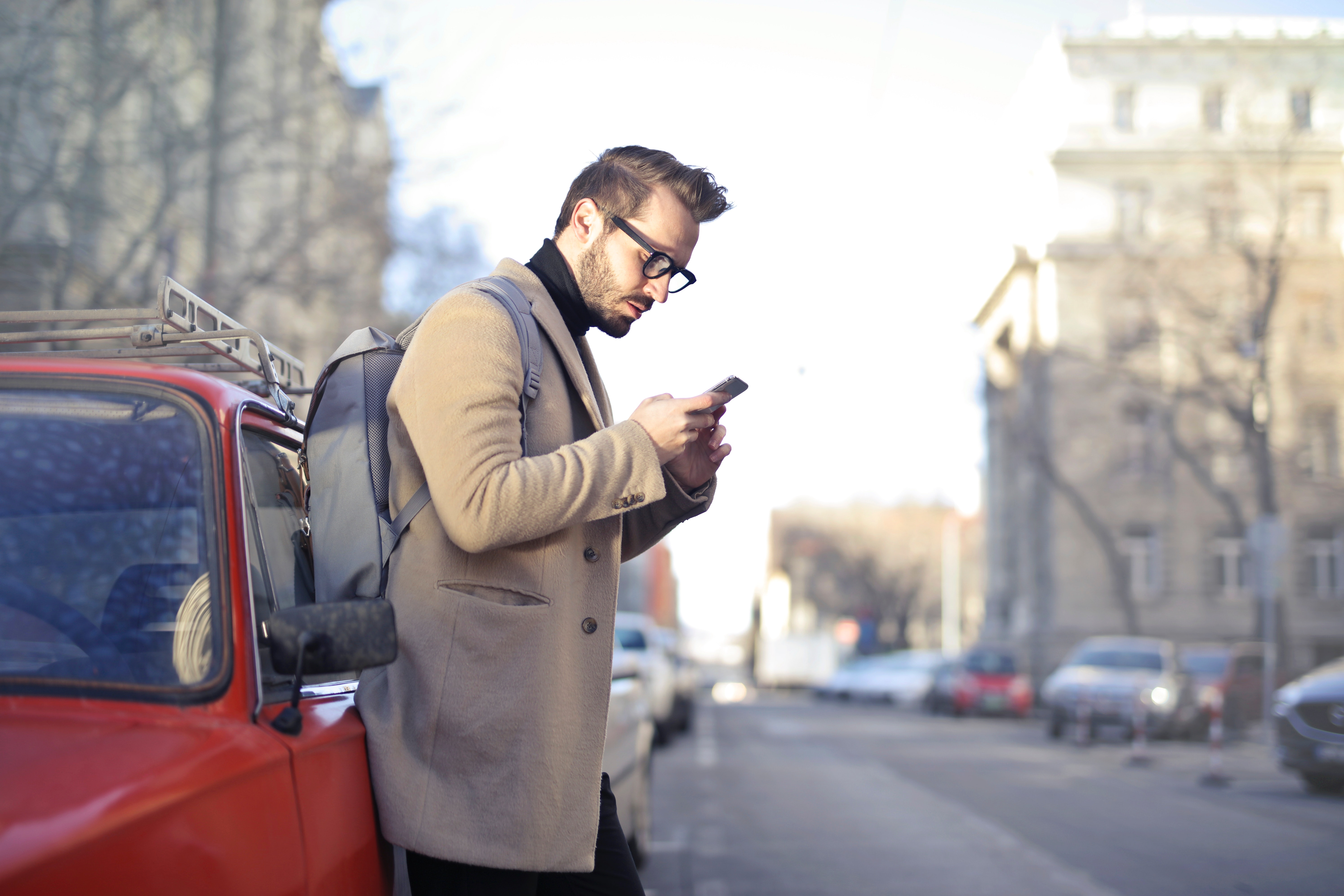 Man in beige coat holding phone leaning on red vehicle photo