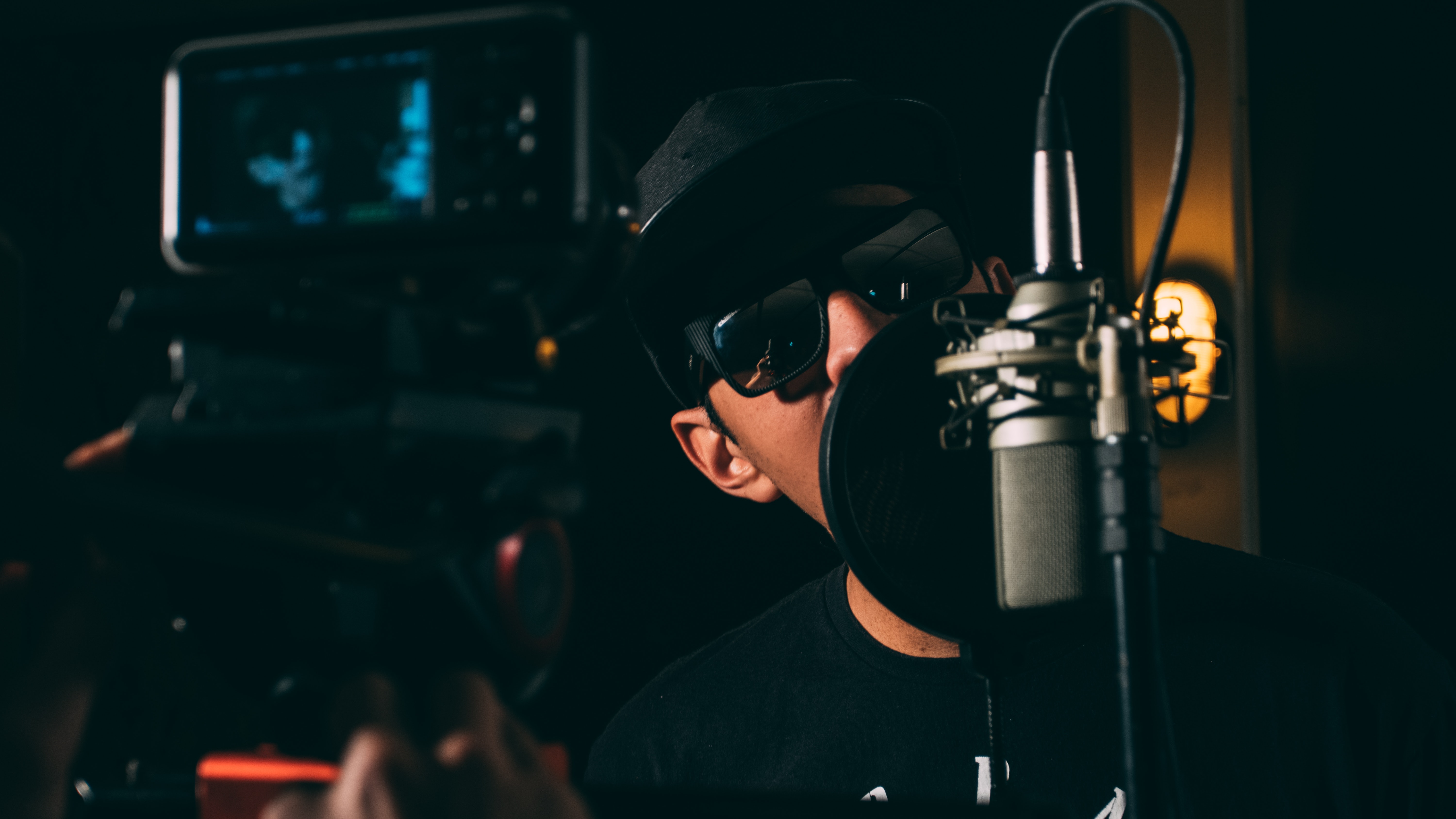 Man in black cap and black framed sunglasses in front recording microphone photo