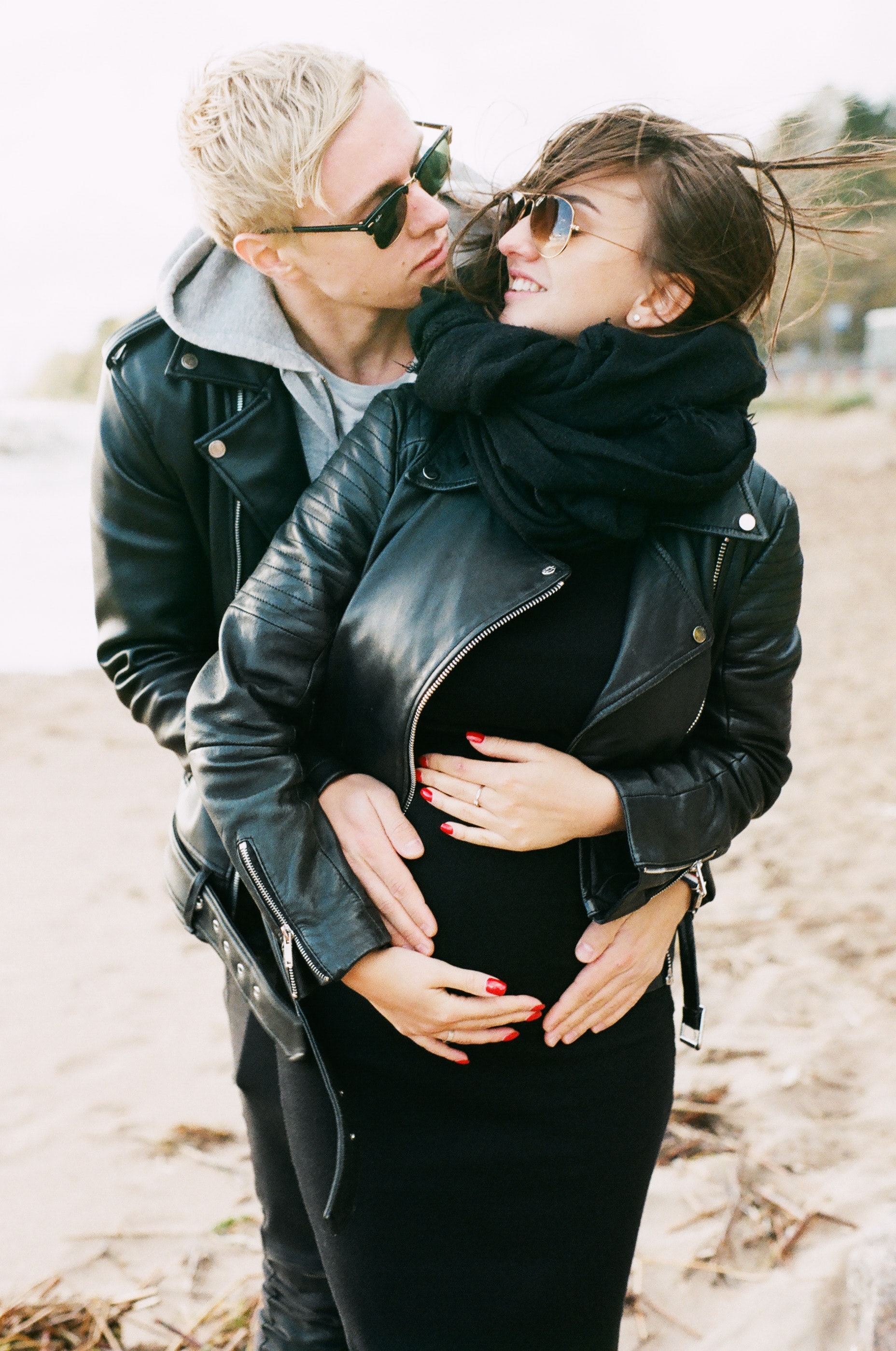 Man in black leather zip jacket hugging woman in black leather zip jacket and black pants standing on sand at daytime photo