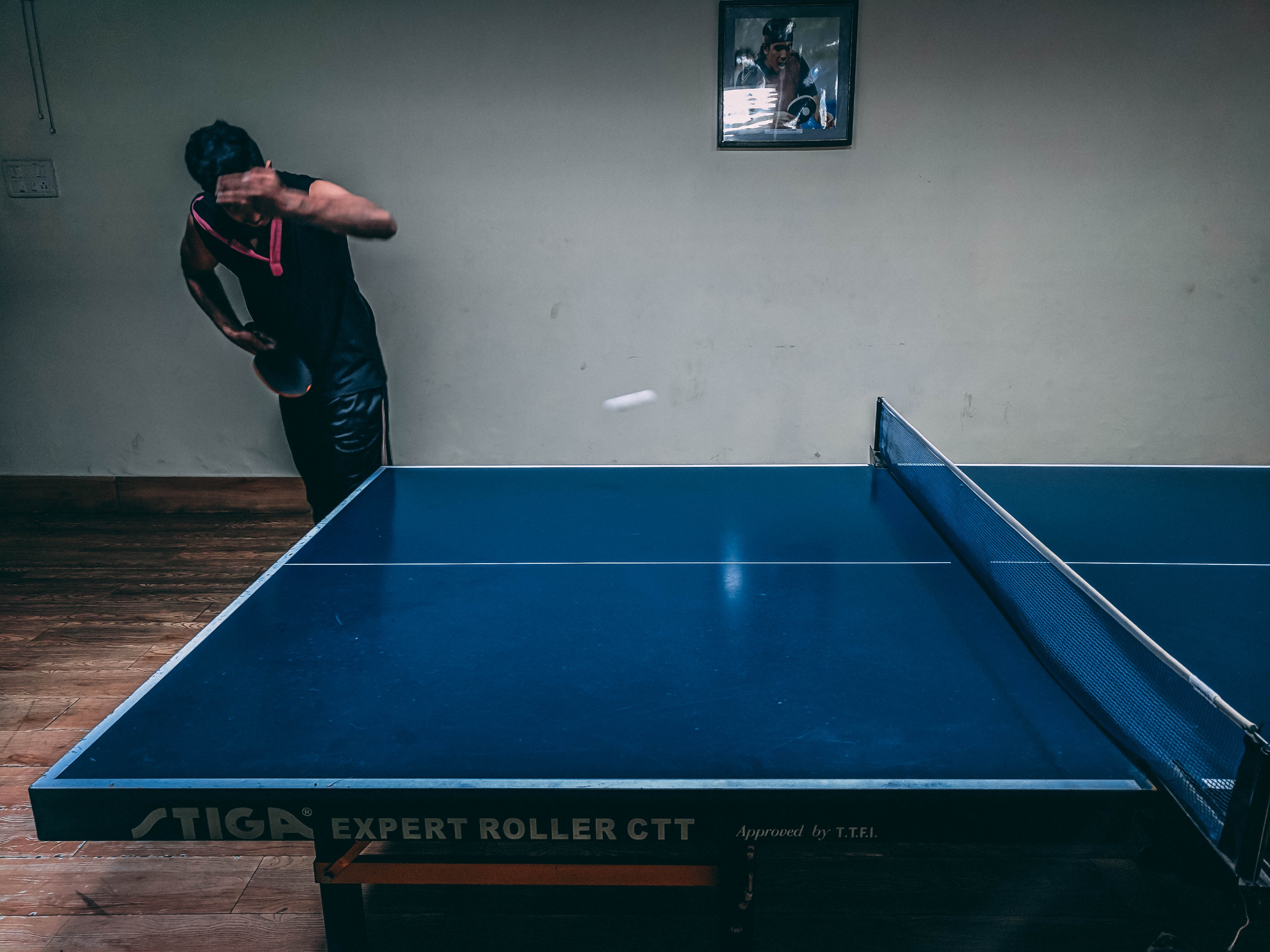 Man in black shirt standing near blue wooden pingpong table photo