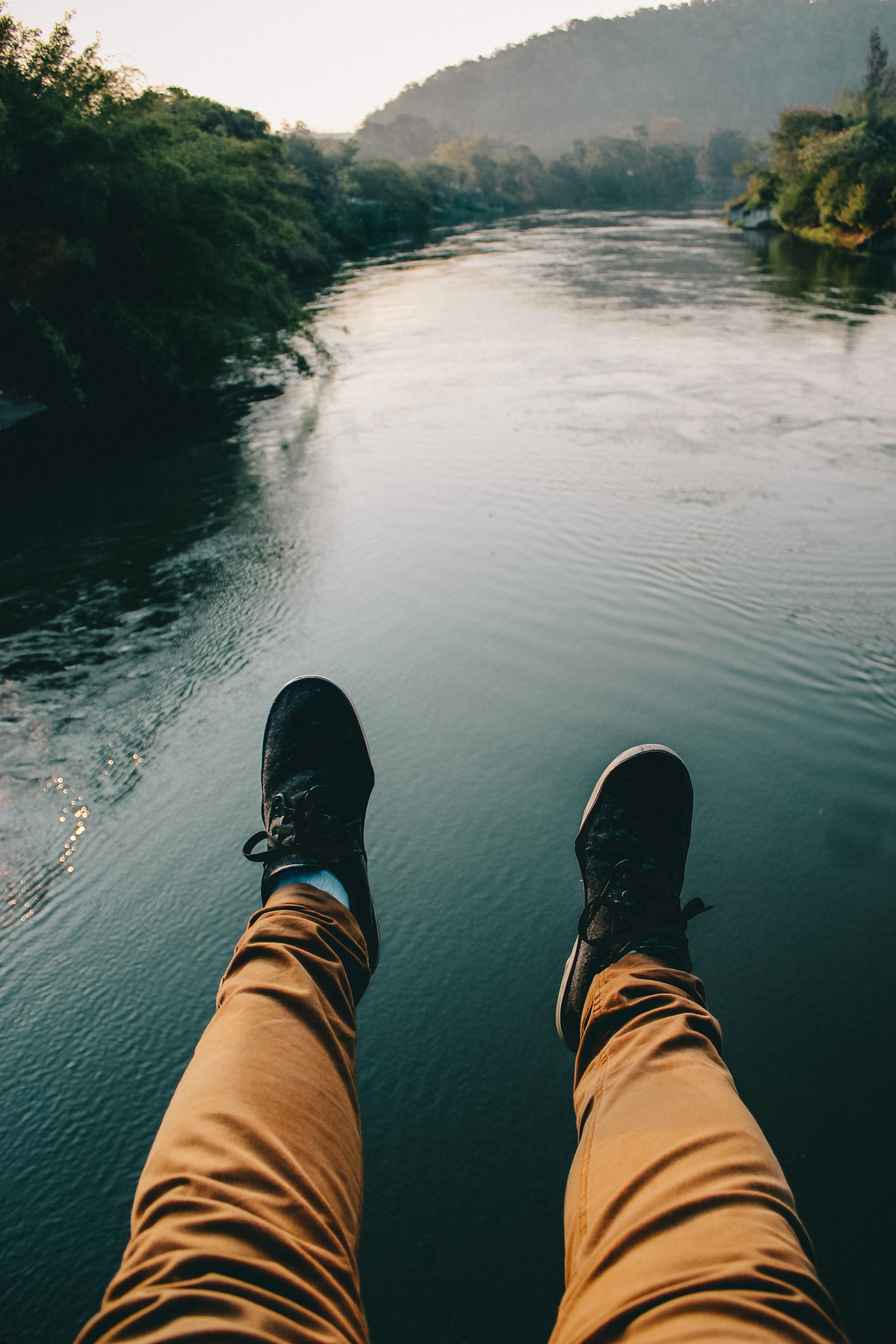 Man in black sneakers and brown pants sitting in front of the river photo