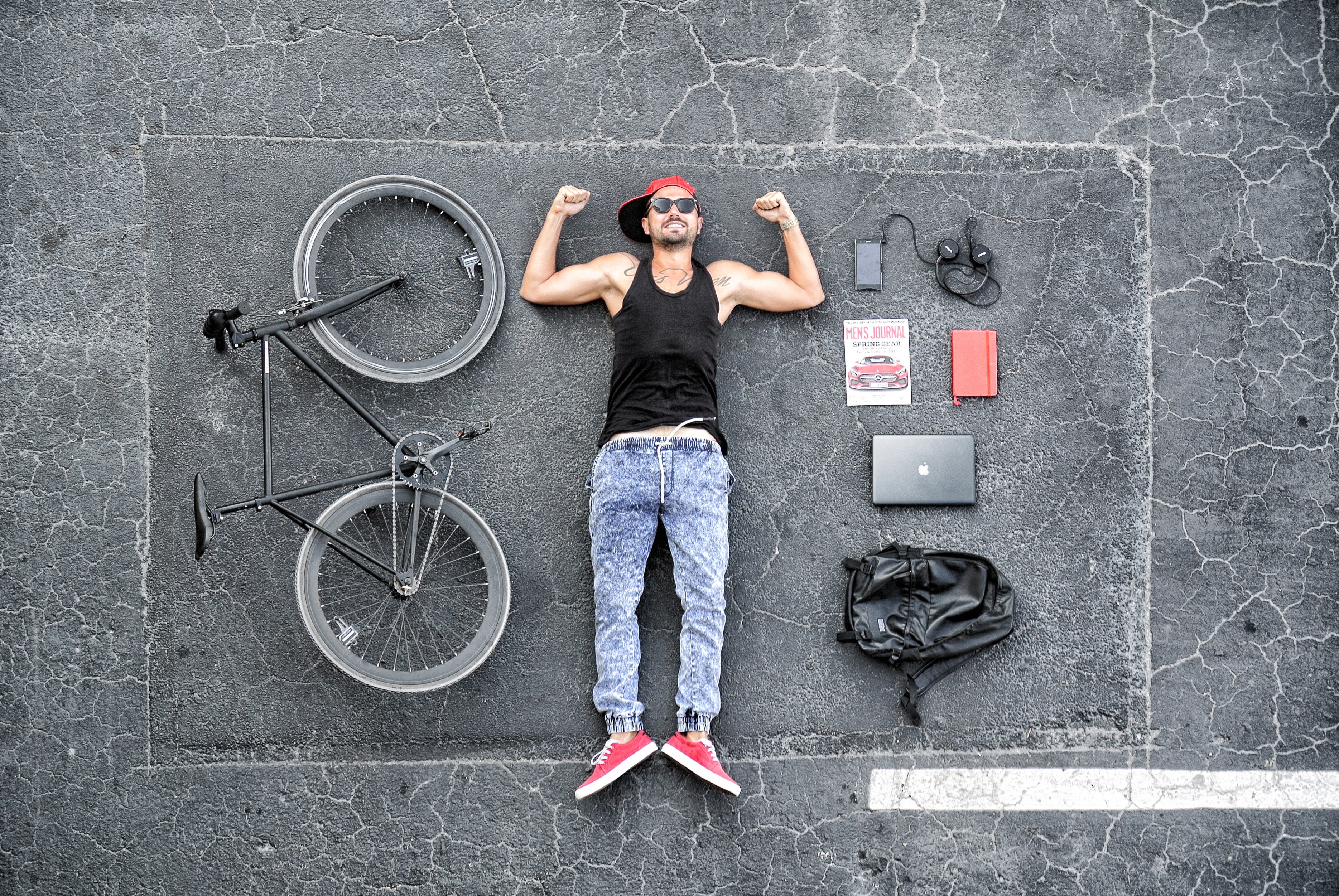 Man in black tank top laying on gray concrete surface near black bike photo