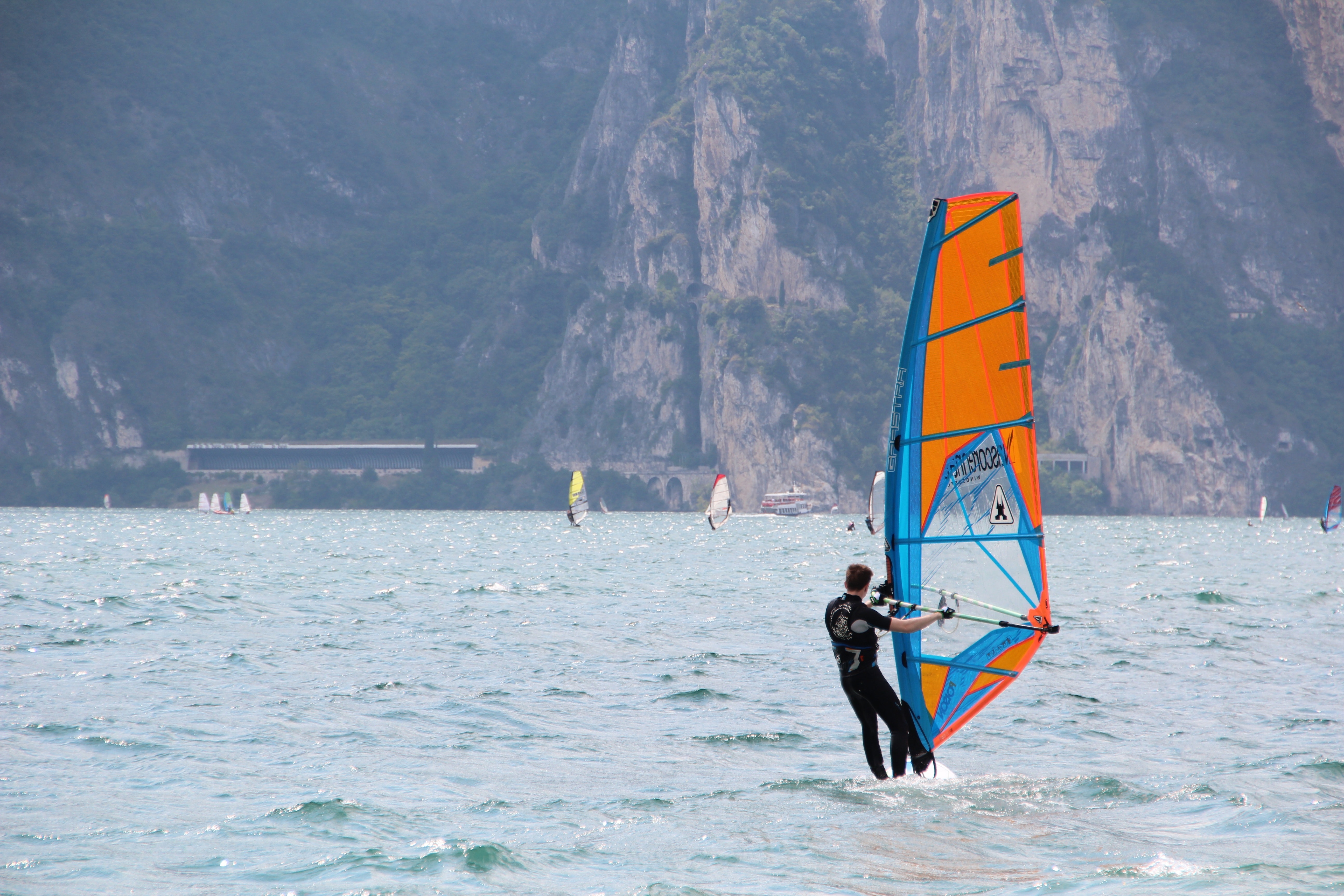 Man in black wetsuit standing on orange and blue sailboat during daytime photo