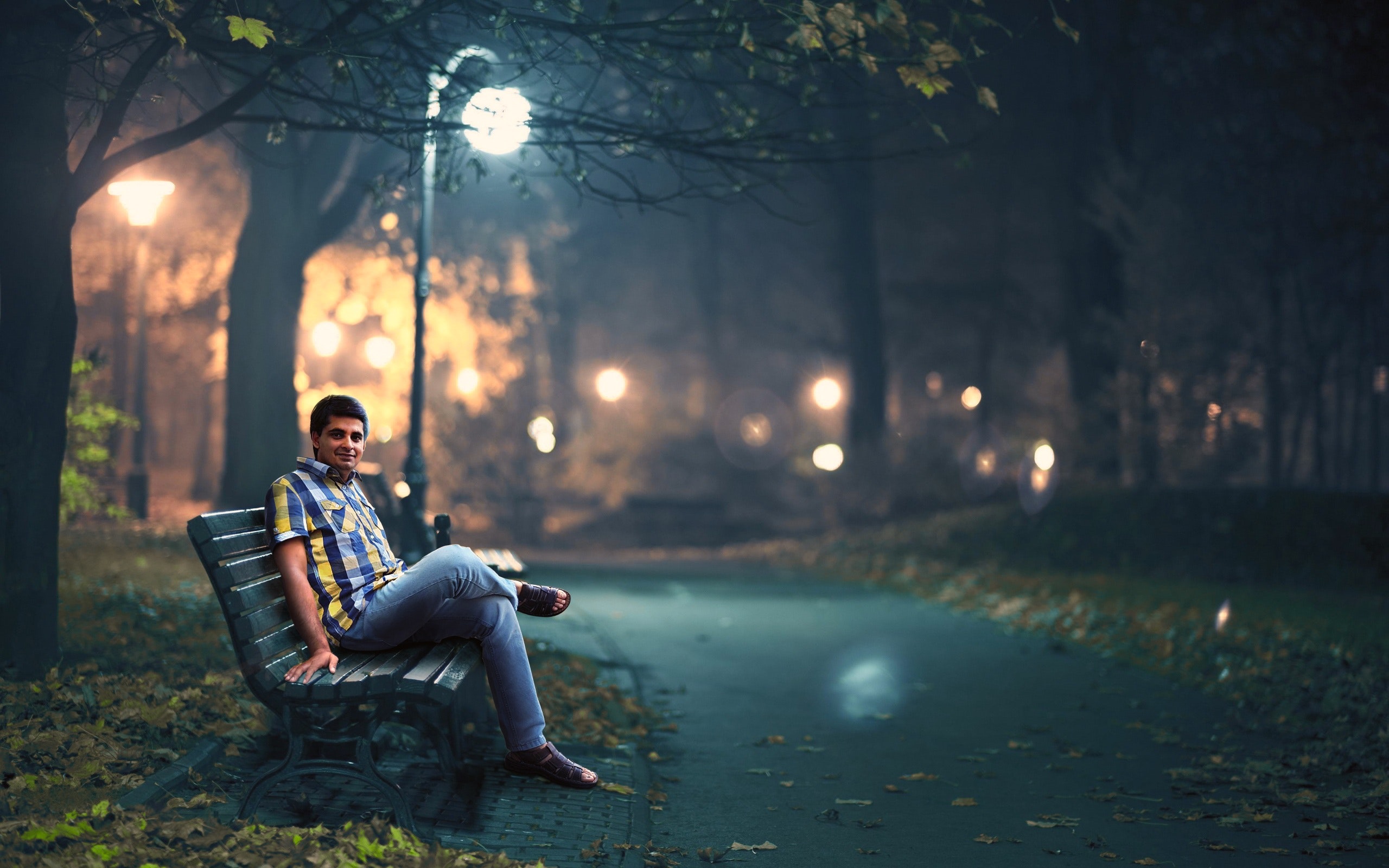 Man in blue denim jeans sitting down by wooden bench near post lamp lighted photo