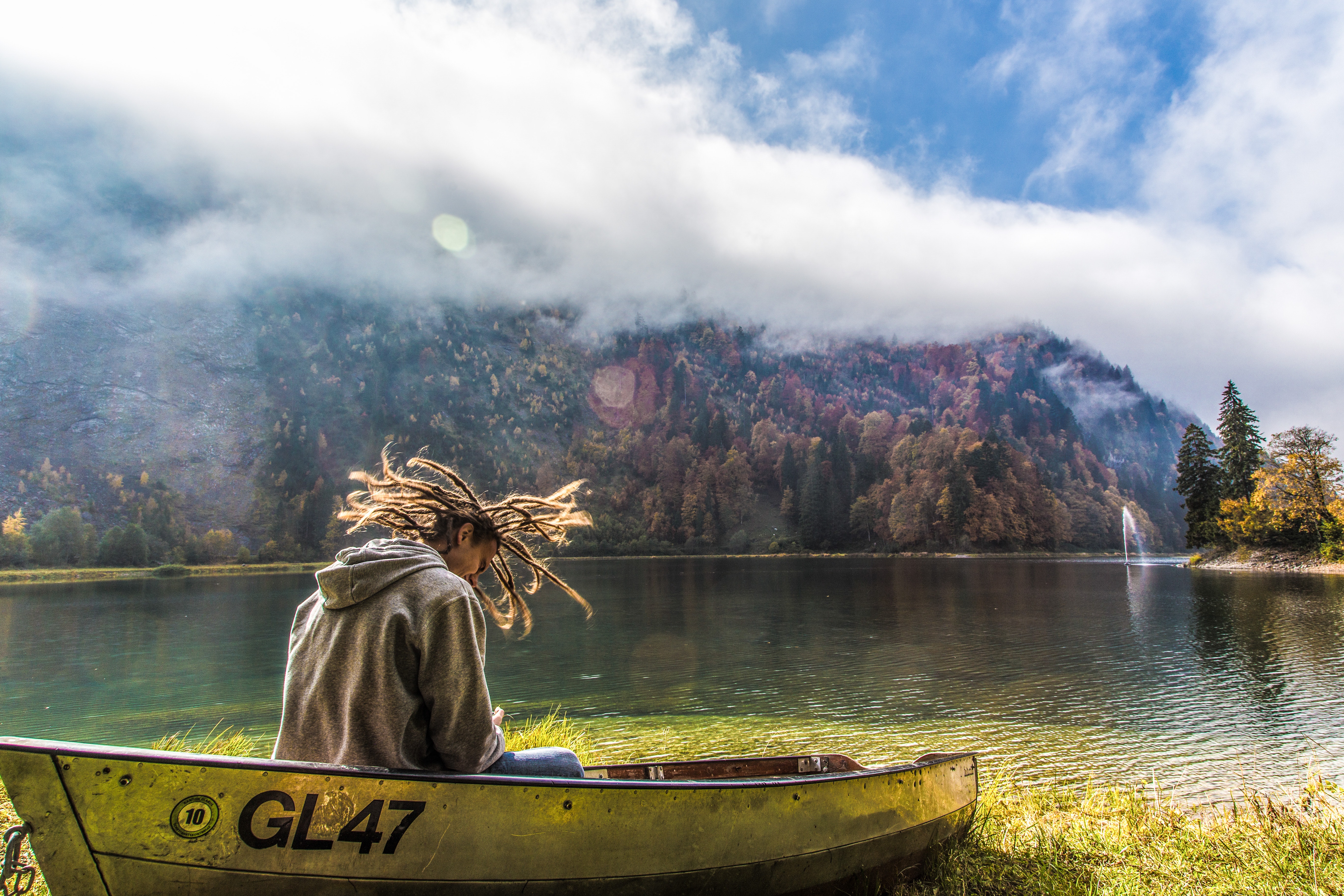 Man in brown hoodie sitting on yellow paddle boat beside lake behind hills during daytime photo