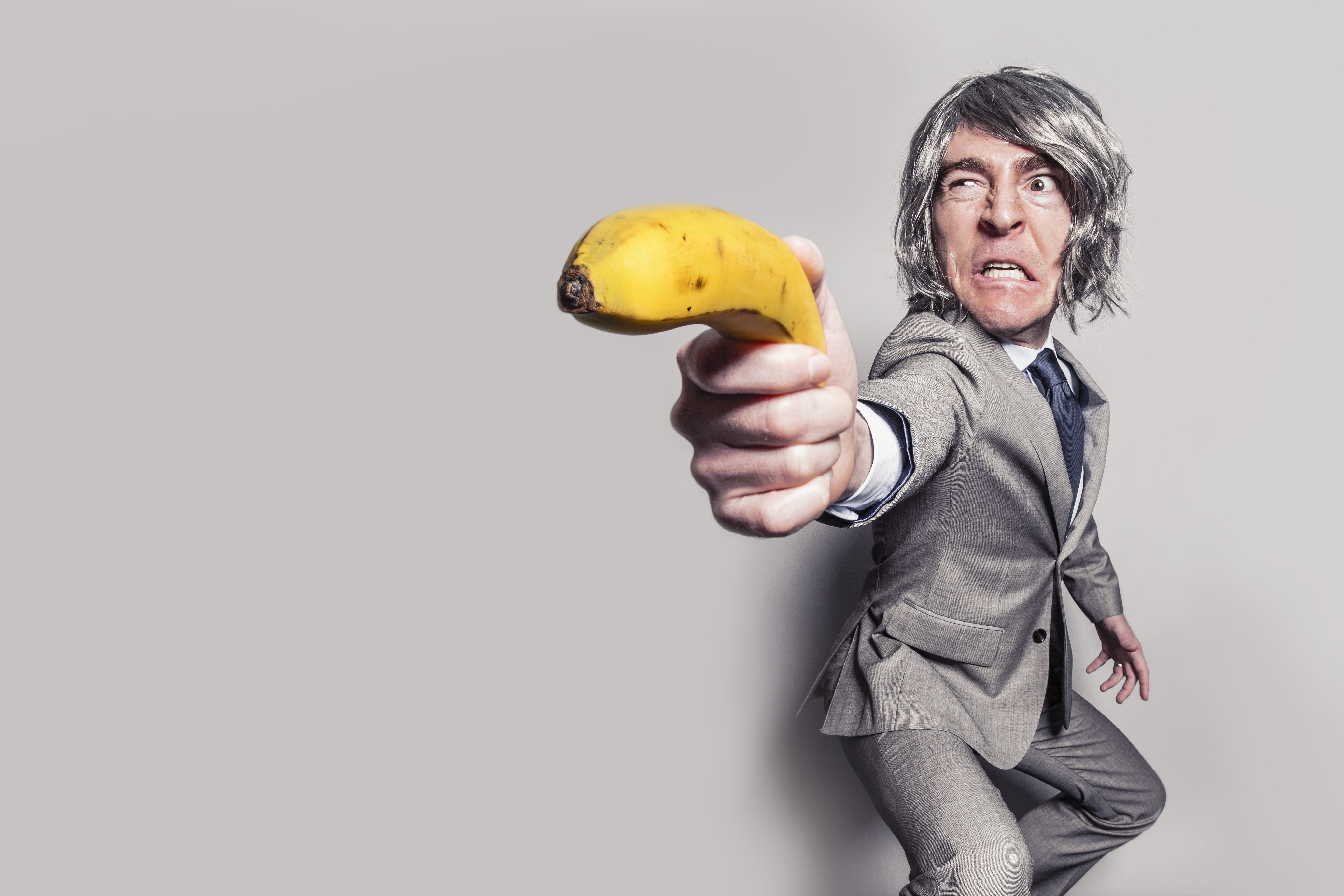 Man in gray suit jacket holding yellow banana fruit while making face photo