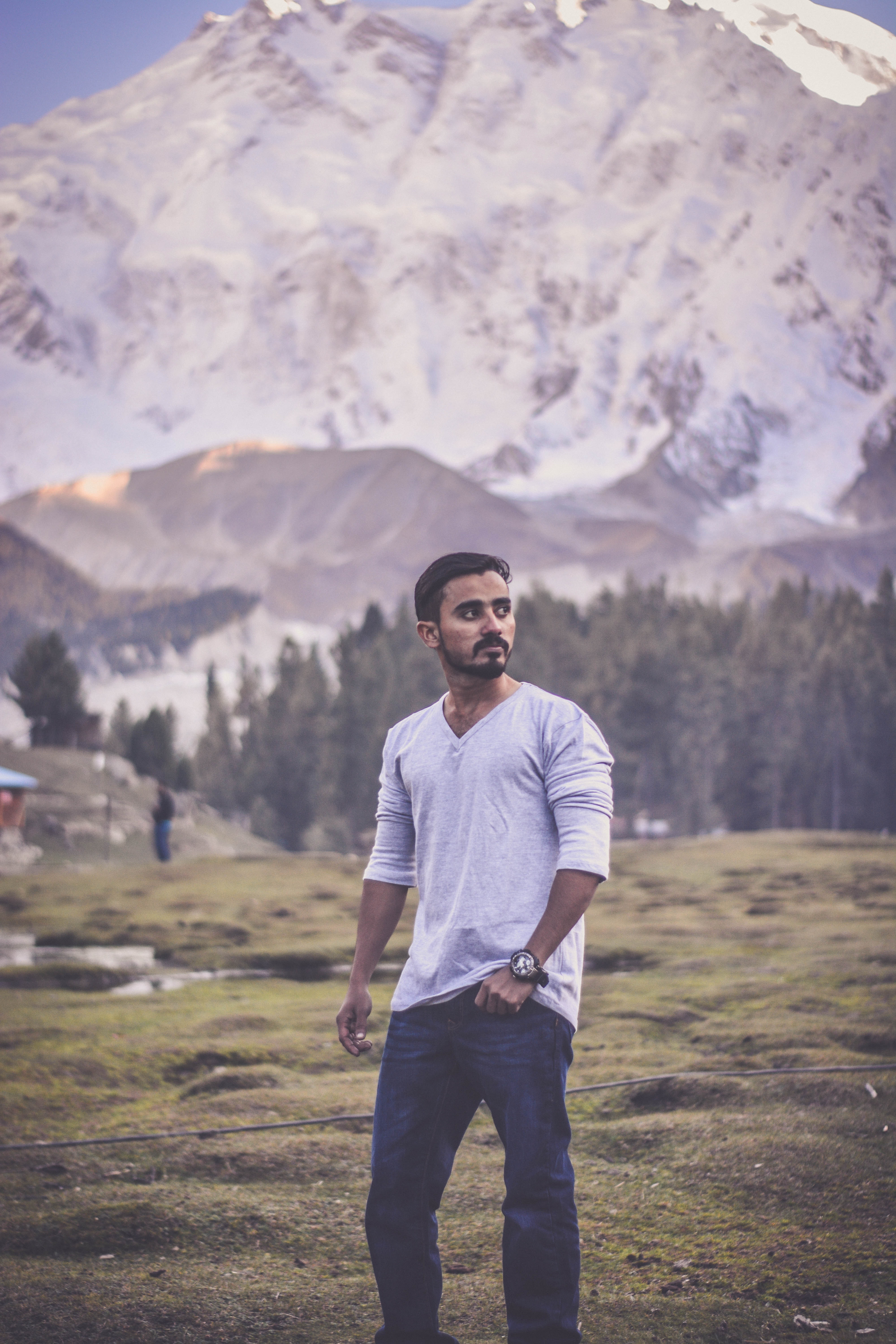 Man in grey v-neck long-sleeved shirt with blue denim jeans behind white mountain photo