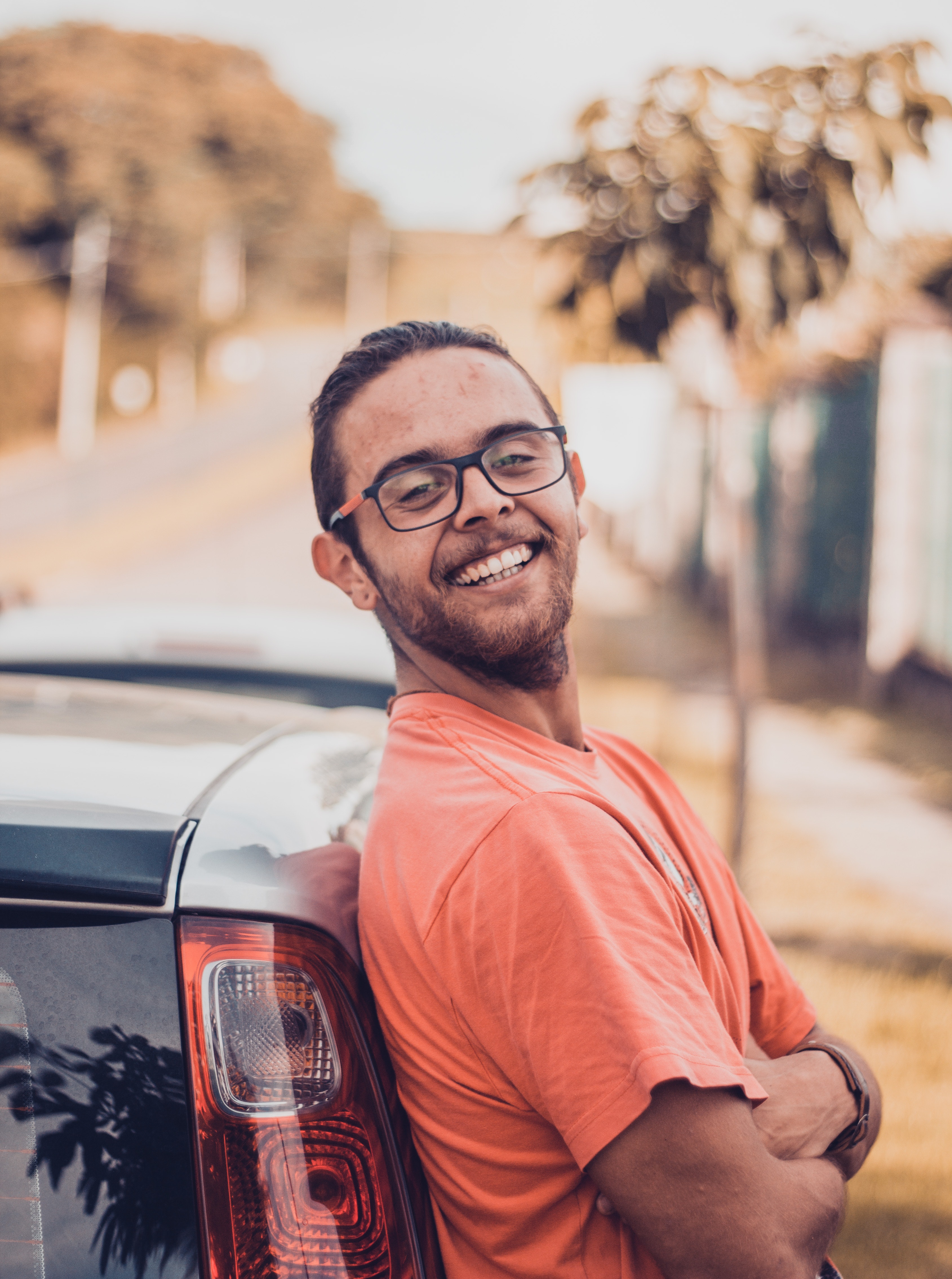 Man in orange t-shirt leaning on a car photo