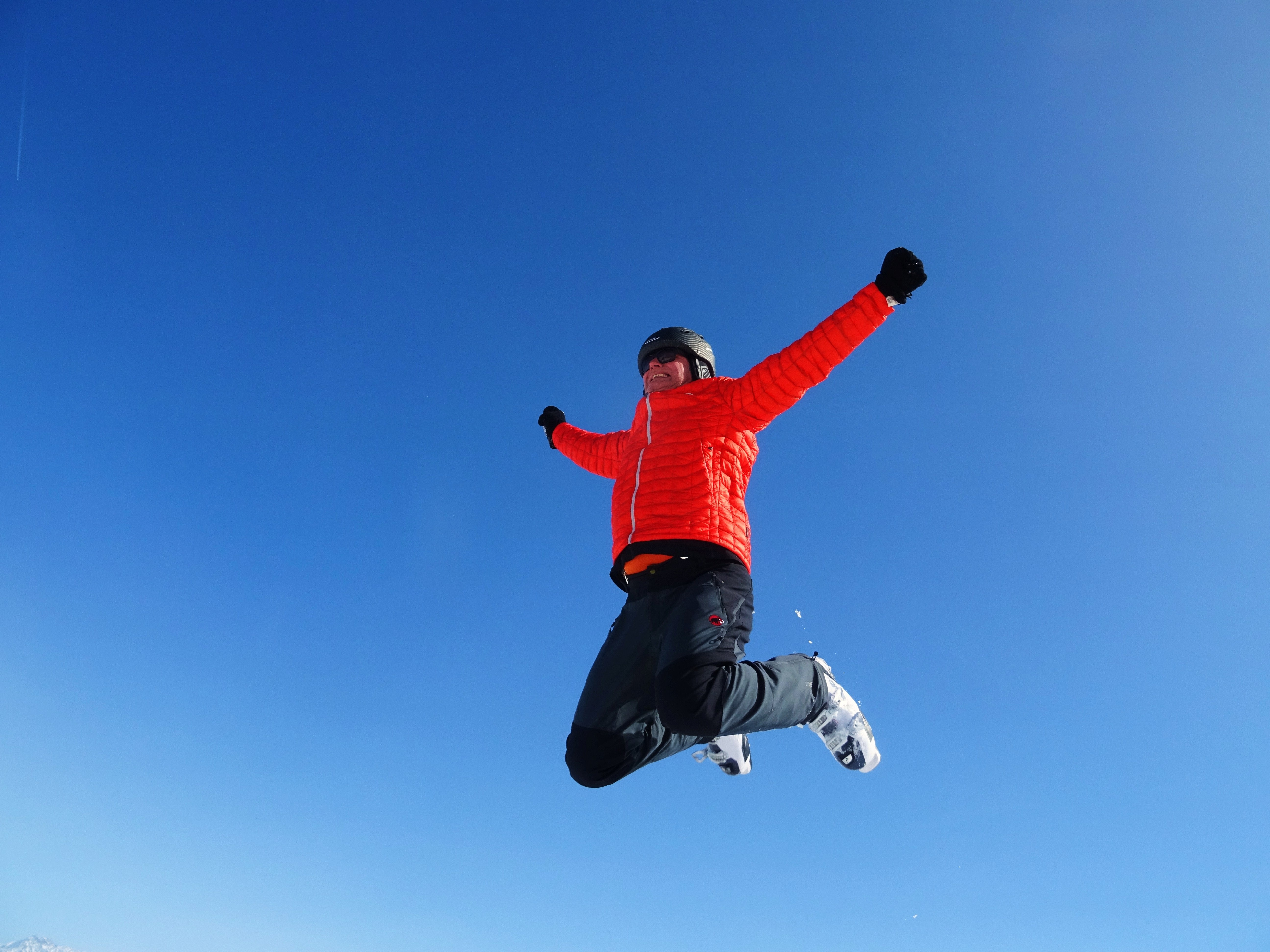 Man in orange zip jacket and black pants jumping under blue sunny sky photo