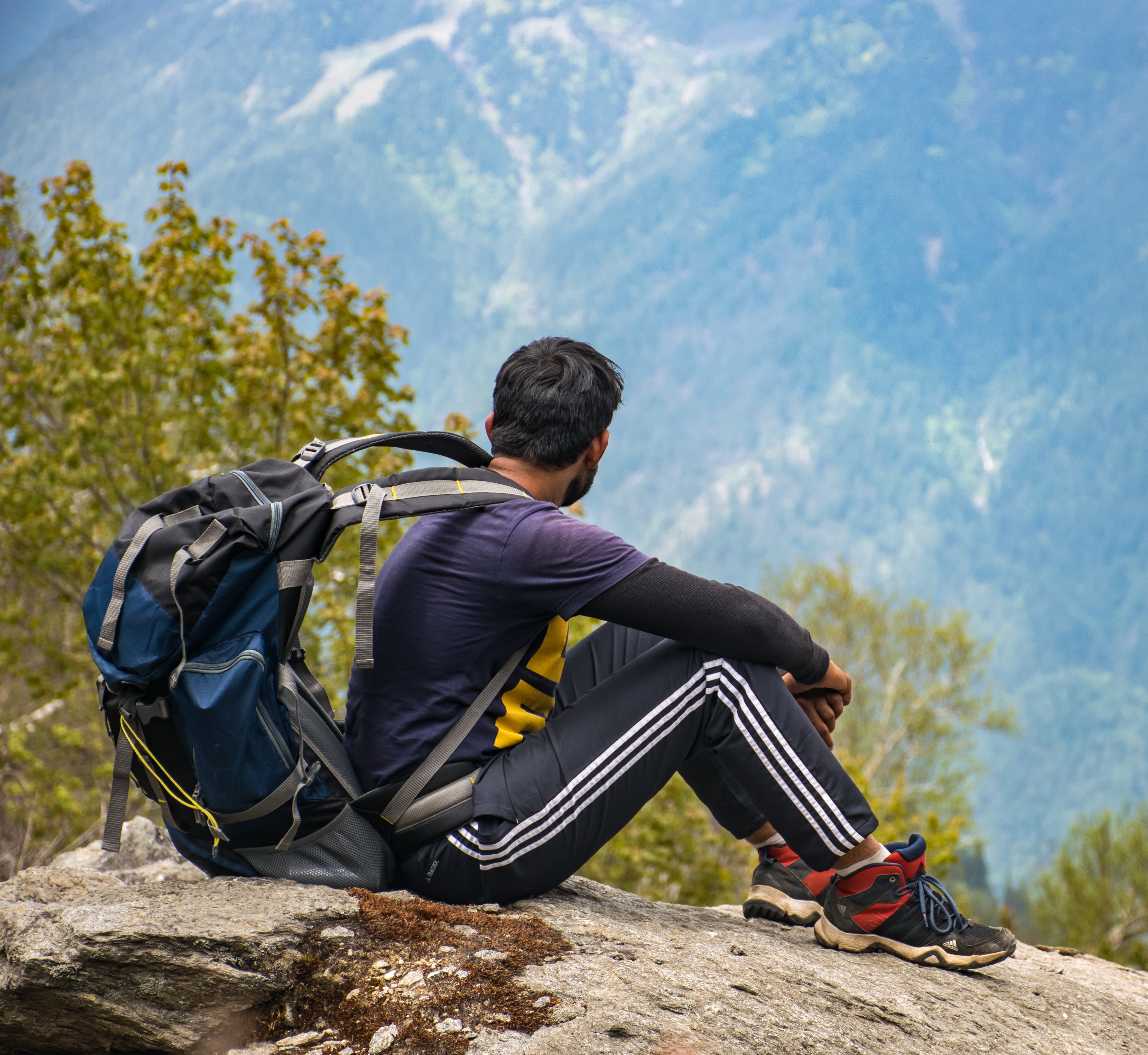 Man in purple t-shirt with blue backpack sitting on gray boulder photo