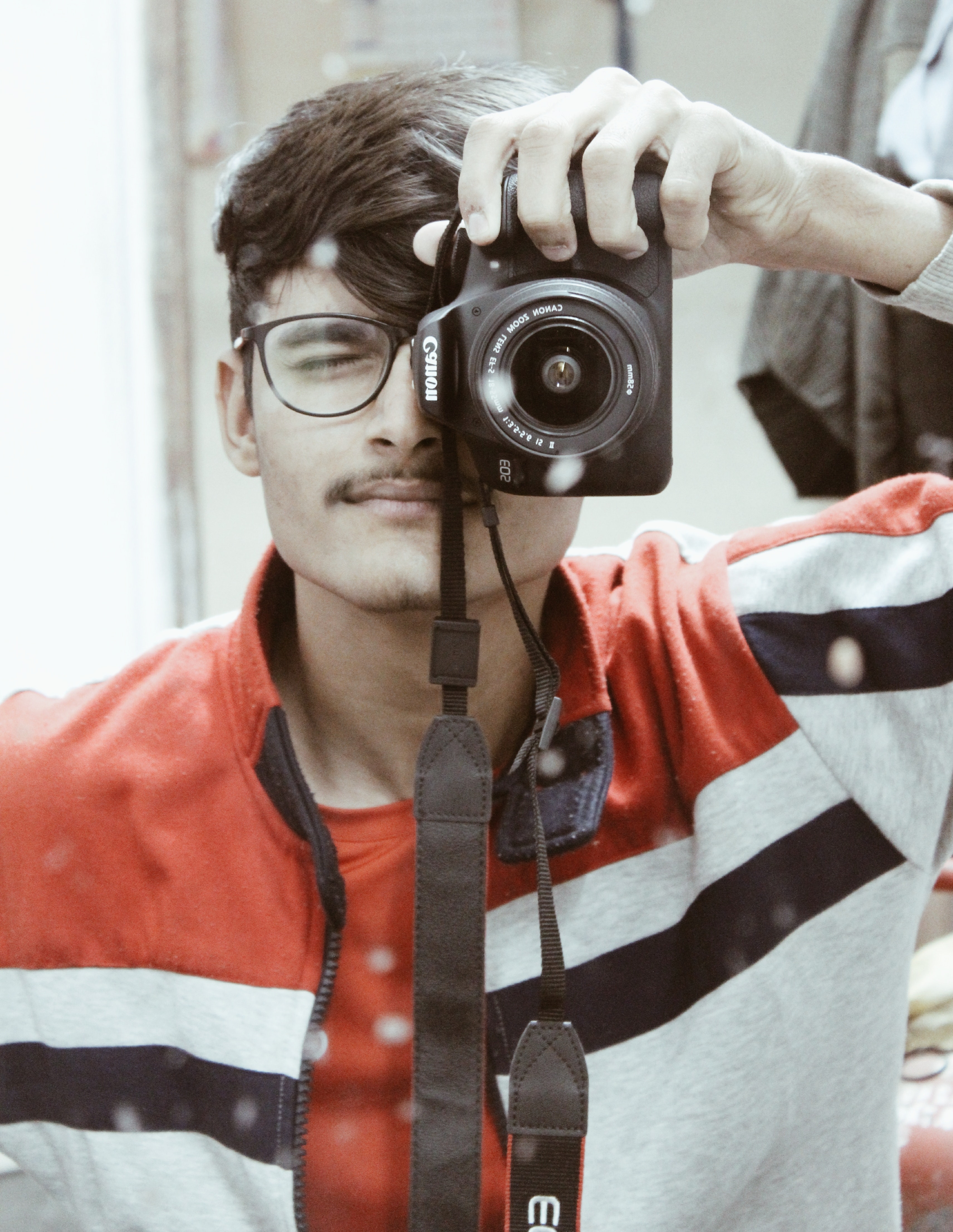 Man in red and white full-zip jacket holding canon dslr camera photo
