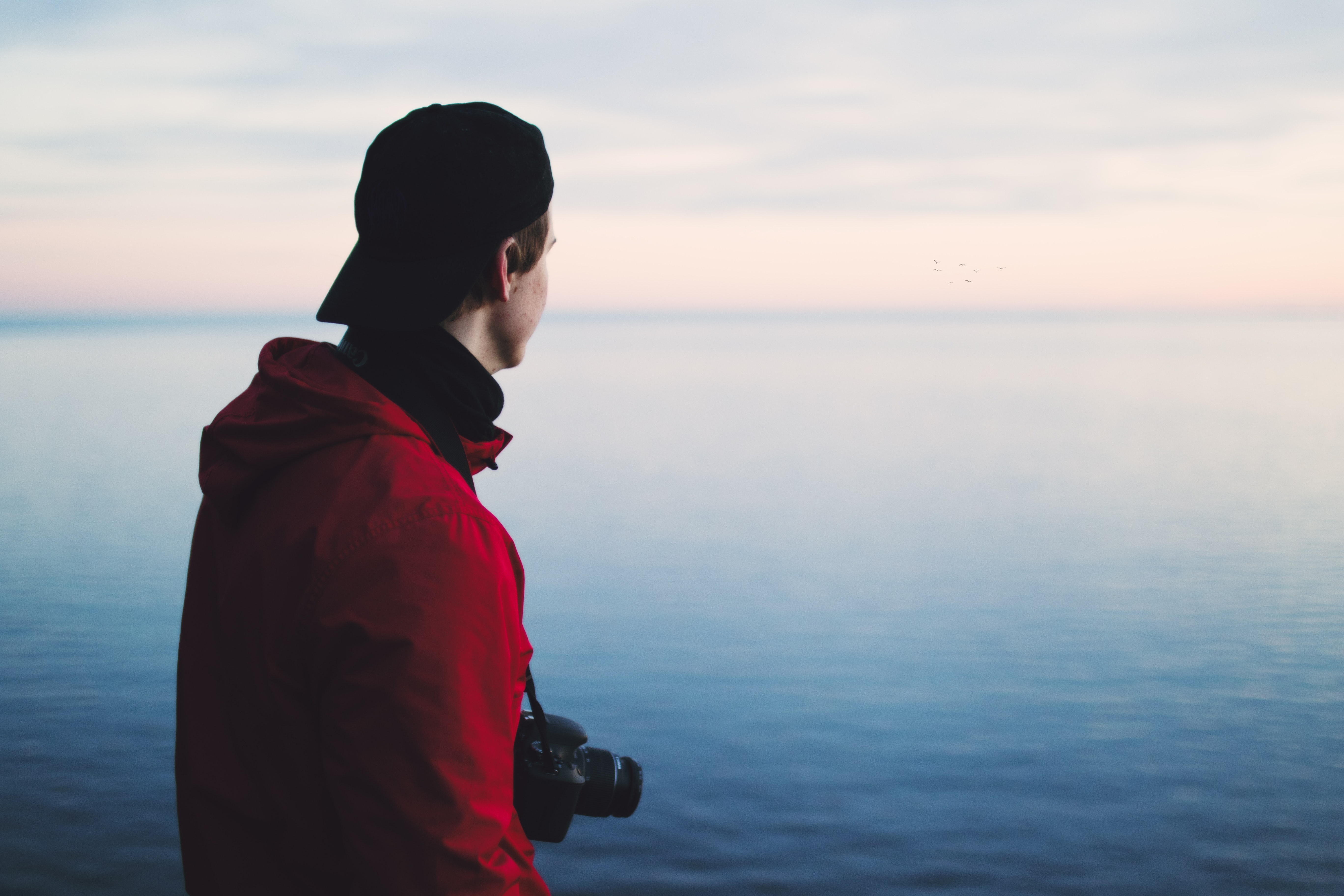 Man in red jacket standing near body of water photo