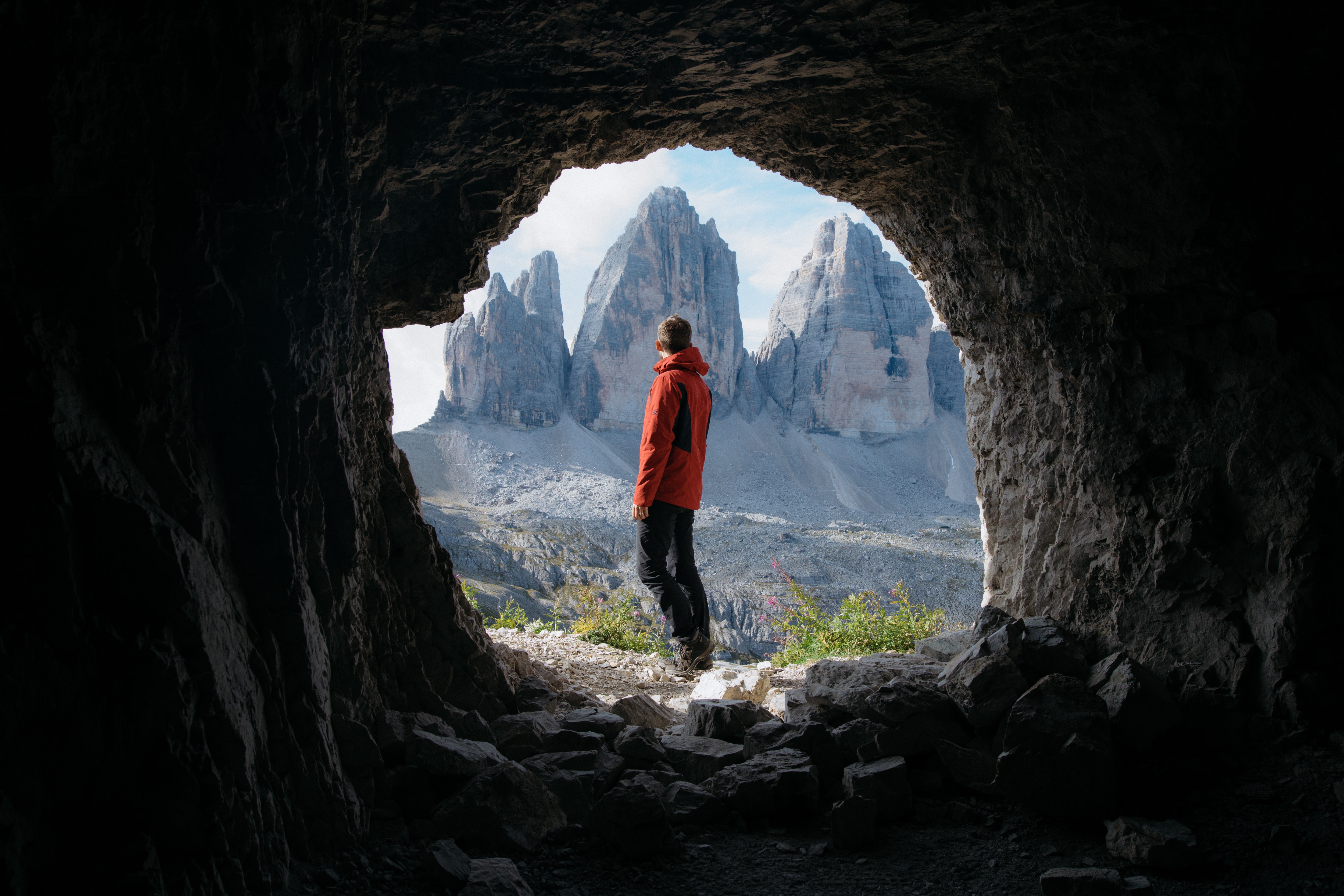 Free Photo Man In Red Jacket Standing Outside Of Cave In Front Of Three Mountains Background Nature Standing Free Download Jooinn