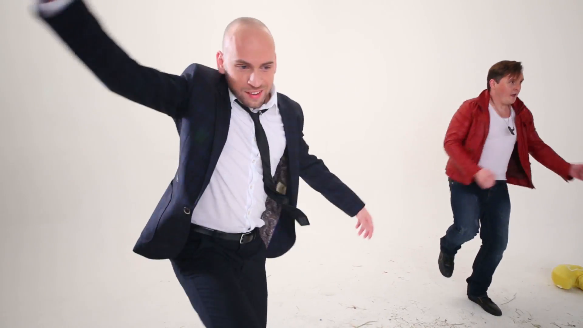 Bald man in suit and man in red jacket dance on floor with hay in ...