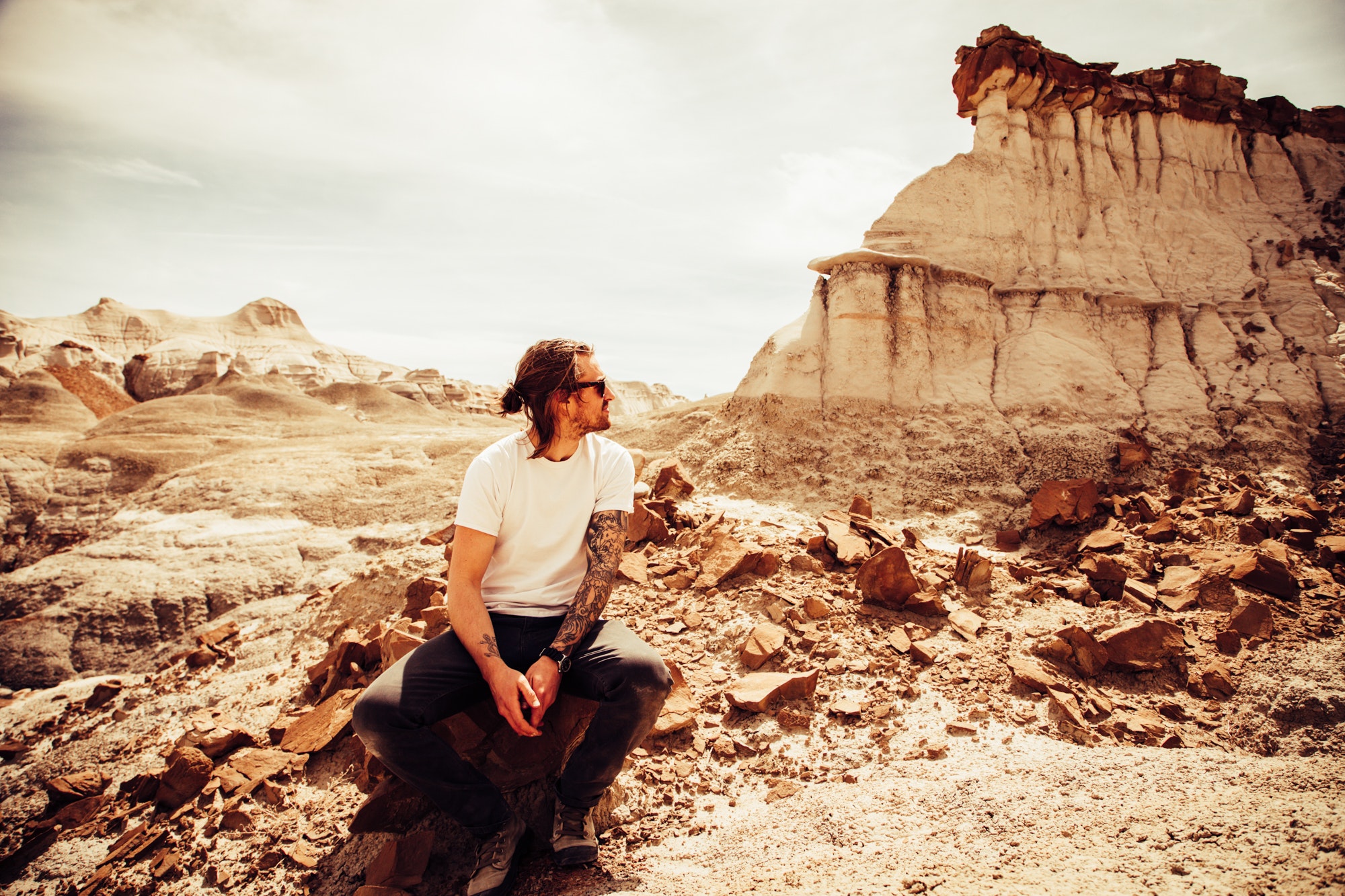 Man in white crew-neck t-shirt and black pants sitting on boulder near cliff photo